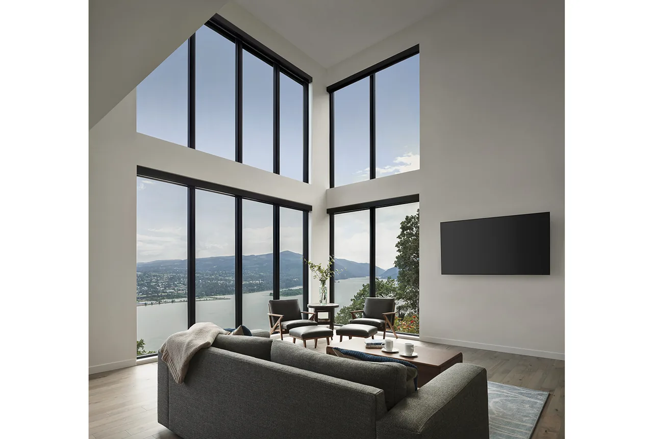Hilltop House living area features two-story corner windows overlooking a river and distant hills.
