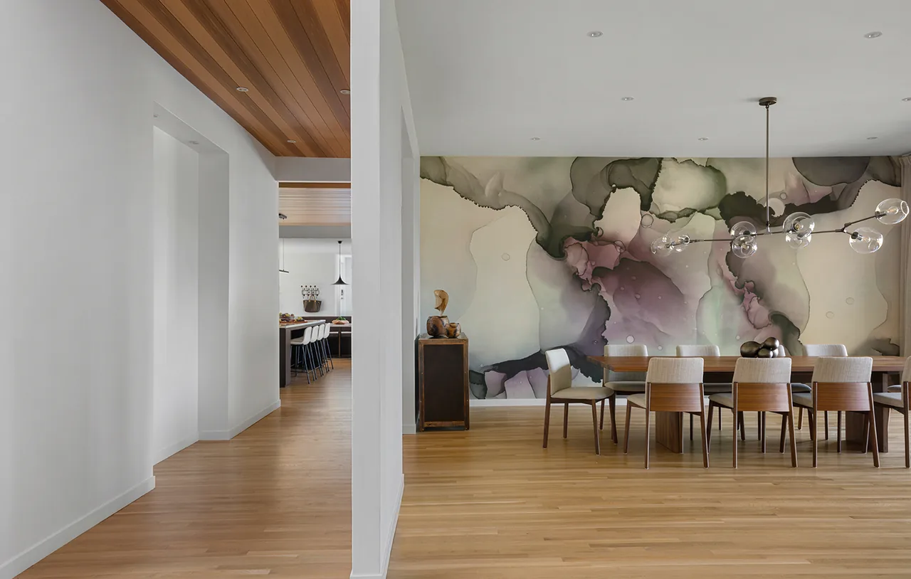 The dining area features a large wooden table, contemporary chairs, and a unique light fixture against an artistic abstract wall.