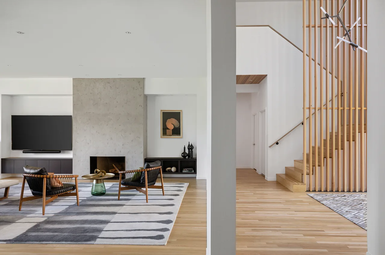 Living room with a concrete fireplace and wood flooring adjacent to a staircase with vertical wood slats.