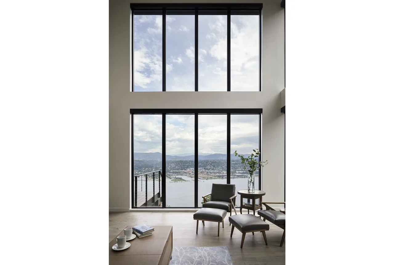 Living room with floor-to-ceiling black-framed windows offering expansive river and city views.
