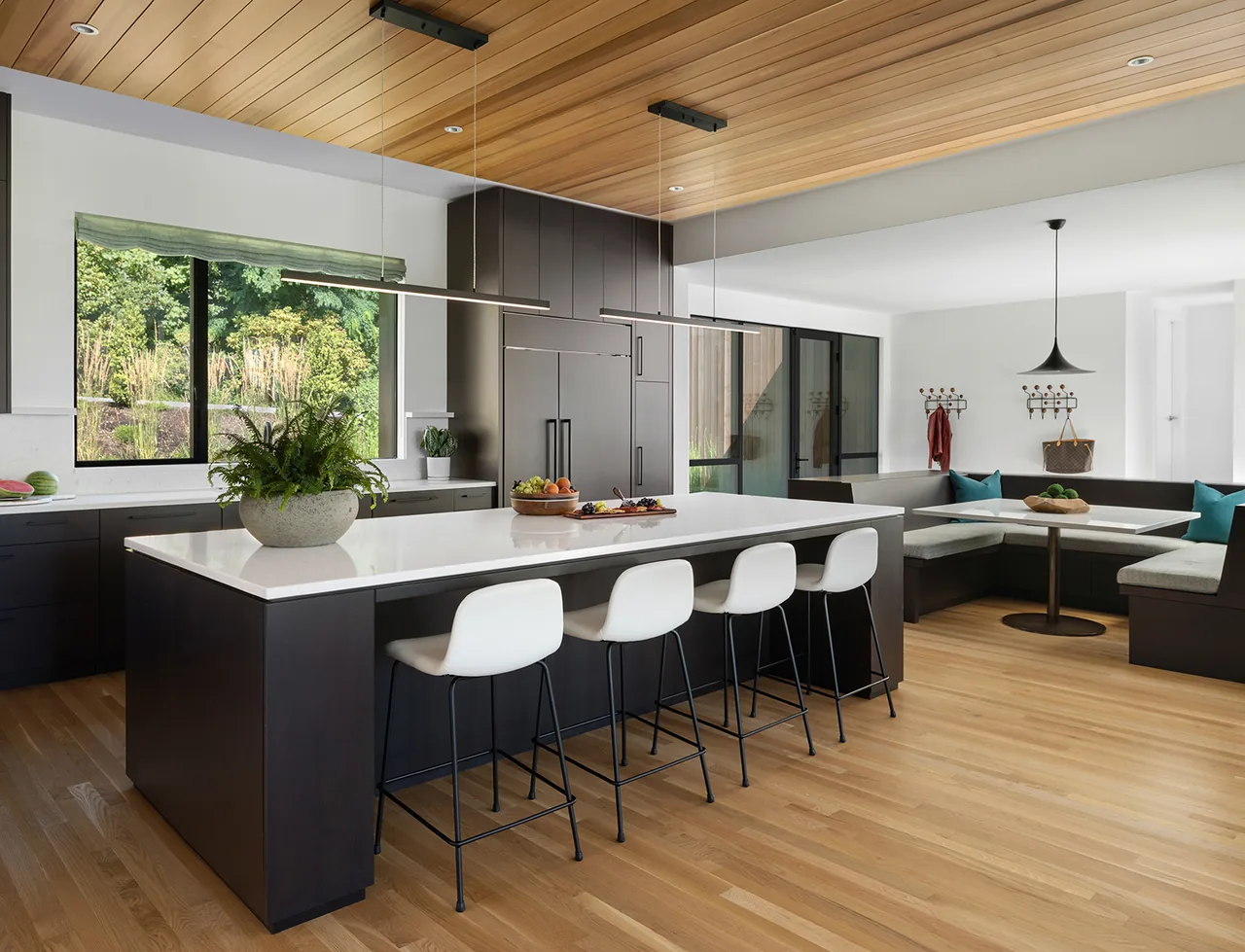 This modern kitchen features a large white island with bar seating, dark cabinetry, and a wood-paneled ceiling.