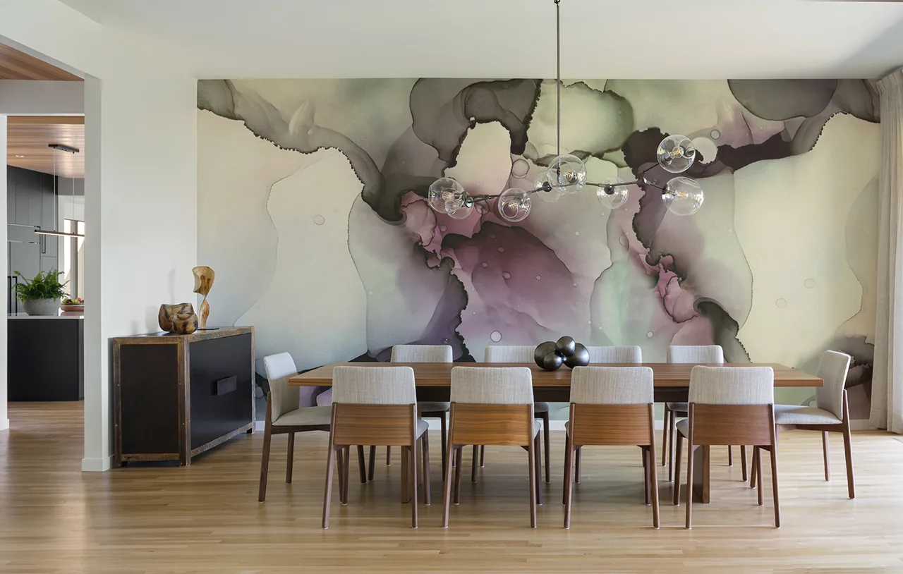 Dining room with a wooden table, upholstered chairs, and an abstract wall mural under a glass globe chandelier.