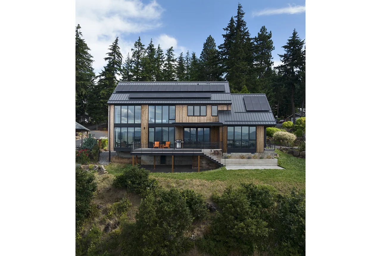 Hilltop House features large glazed walls, vertical wood siding, and standing seam metal roofing with solar panels.