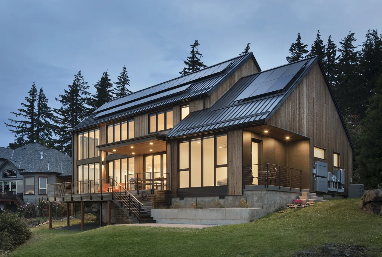 Hilltop House features vertical wood siding, metal standing seam roofs with solar panels, and extensive floor-to-ceiling glazing.