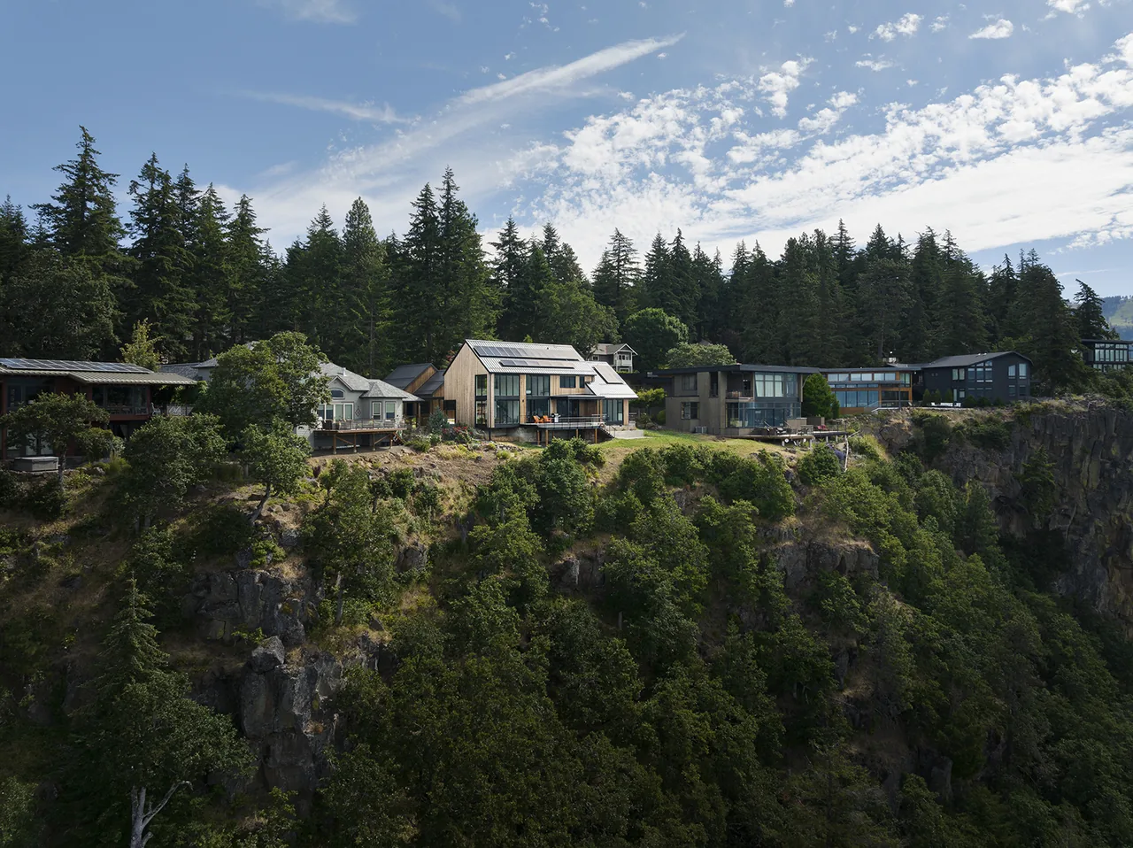 Hilltop House and neighboring homes perched on a forested cliff with a river view and solar panels visible on the roof.
