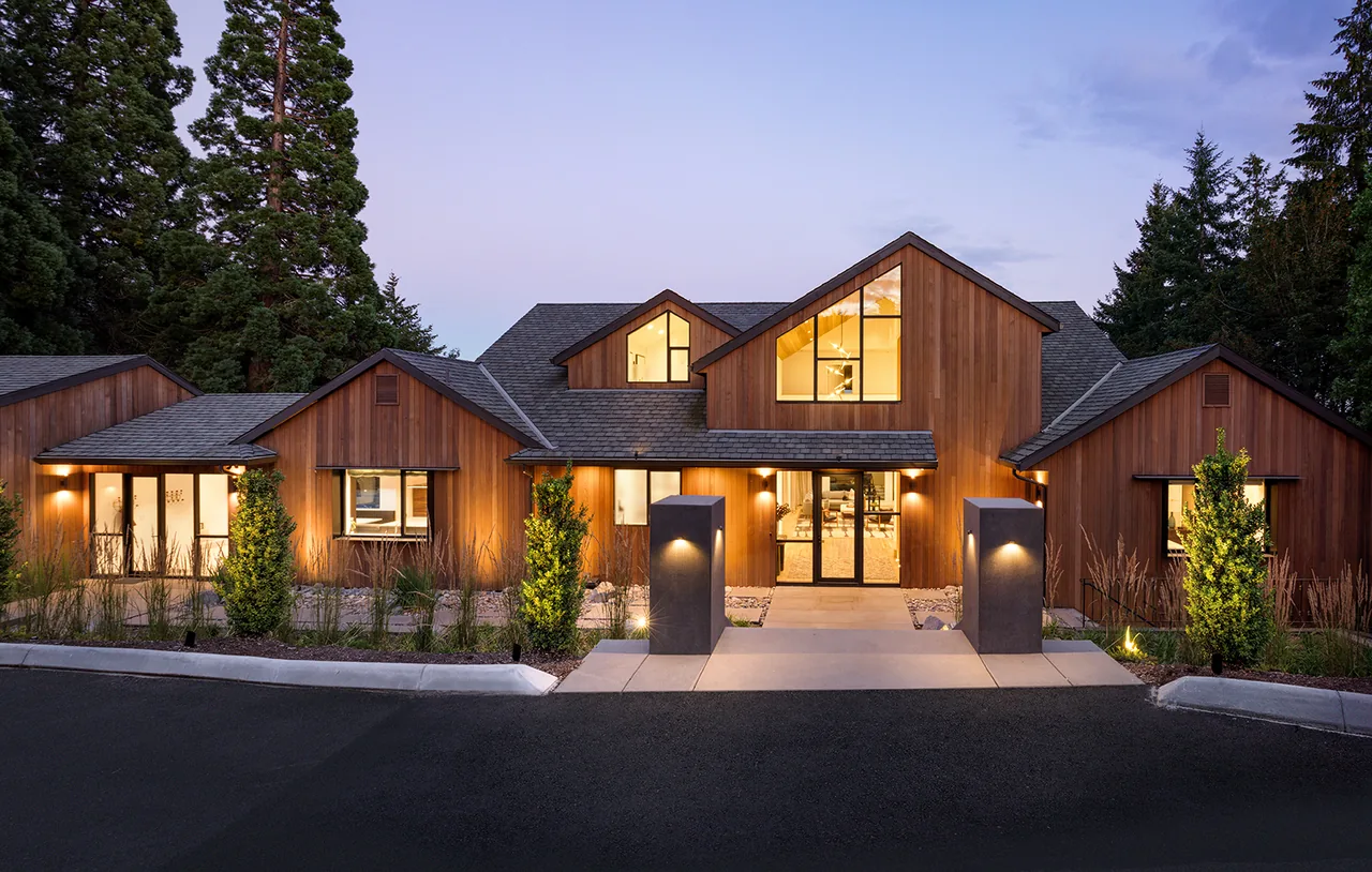 The Hilltop House features warm wood siding and large two-story windows under multiple gable roofs in a wooded setting.