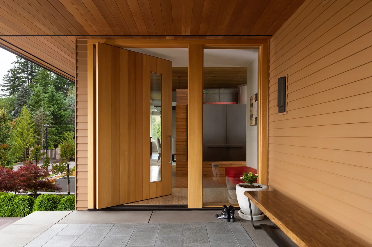 Front entrance of Highlands Loop Residence features a wide wooden pivot door with glass inset and covered porch.