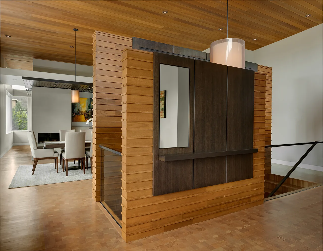 Dining area with white upholstered chairs, wooden floor and ceiling, and a decorative wooden wall panel.