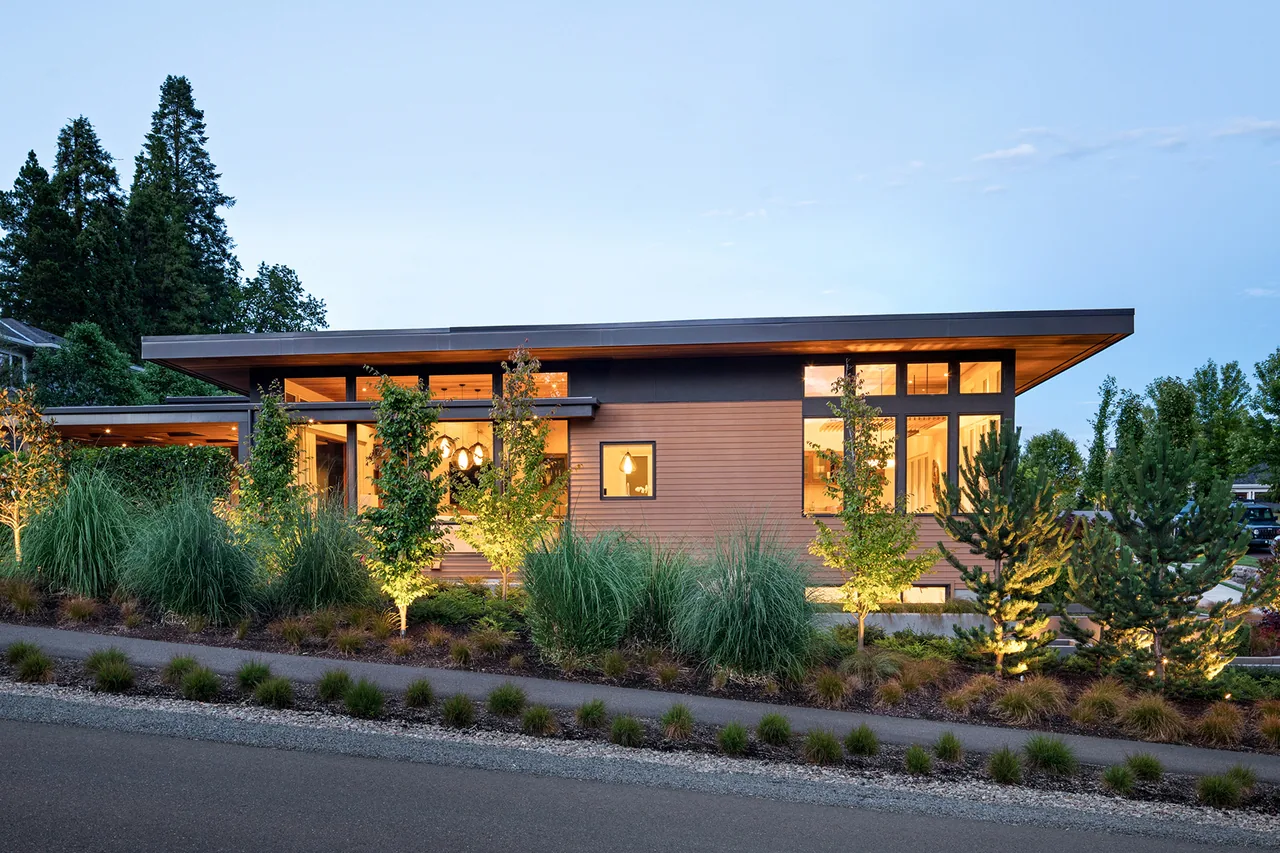Highlands Loop Residence features wood siding and an overhanging flat roof with exterior lighting highlighting landscaping.
