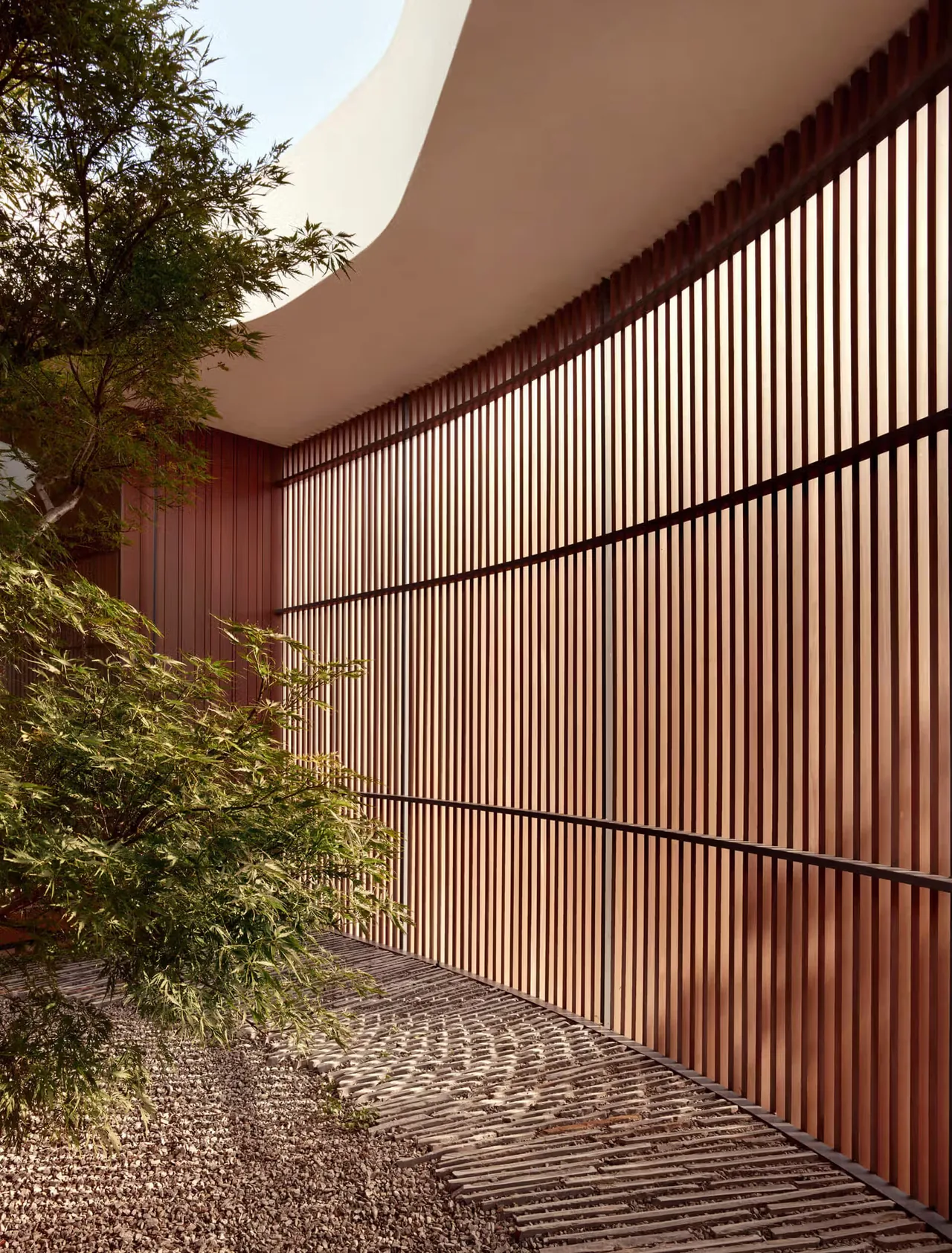 Curved vertical wood slat wall creating an outdoor semi-enclosed space with gravel ground cover.
