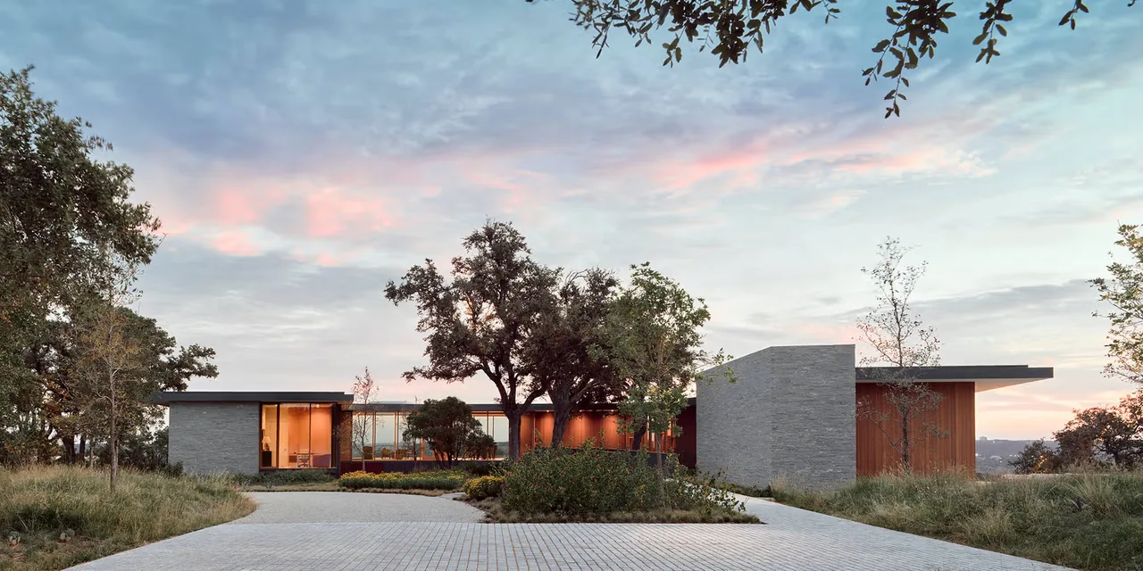 City Park Residence in Austin features a modern flat-roof design with stone walls and wood siding framed by mature trees.