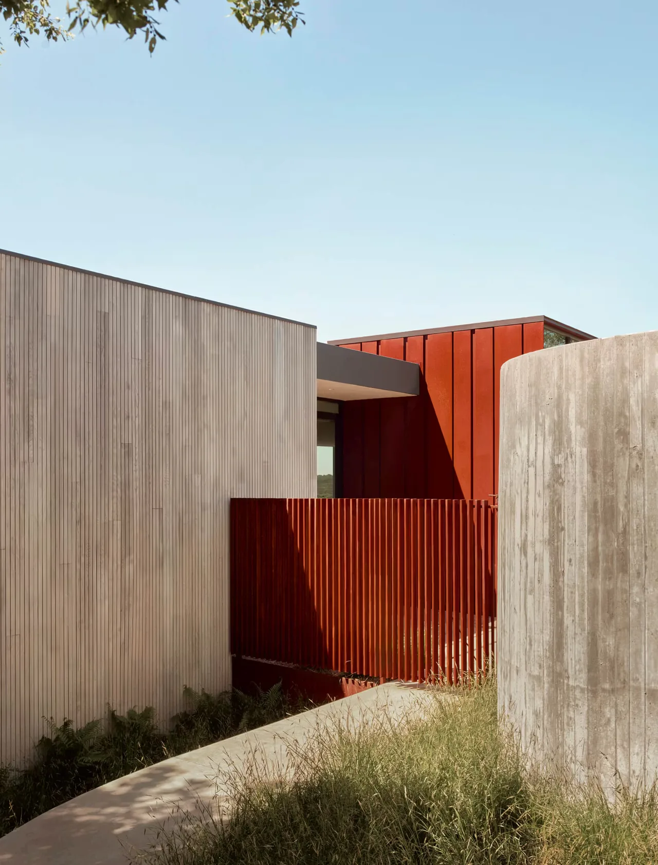 Barton Hills Residence features contrasting materials including wood paneling, red metal siding, and a curved concrete perimeter wall.
