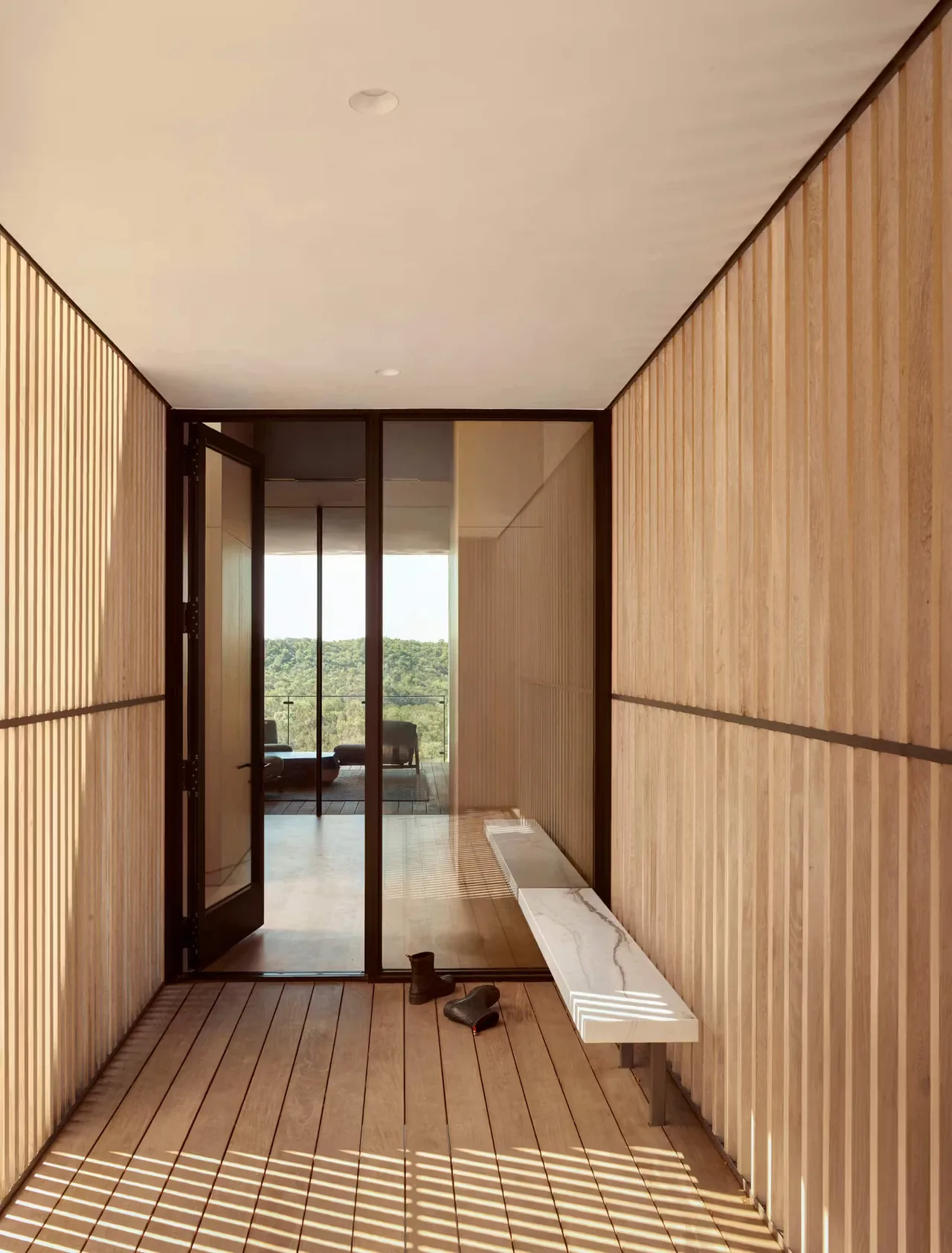 Covered entry with wood slat walls and floor, featuring a glass door and a marble bench.