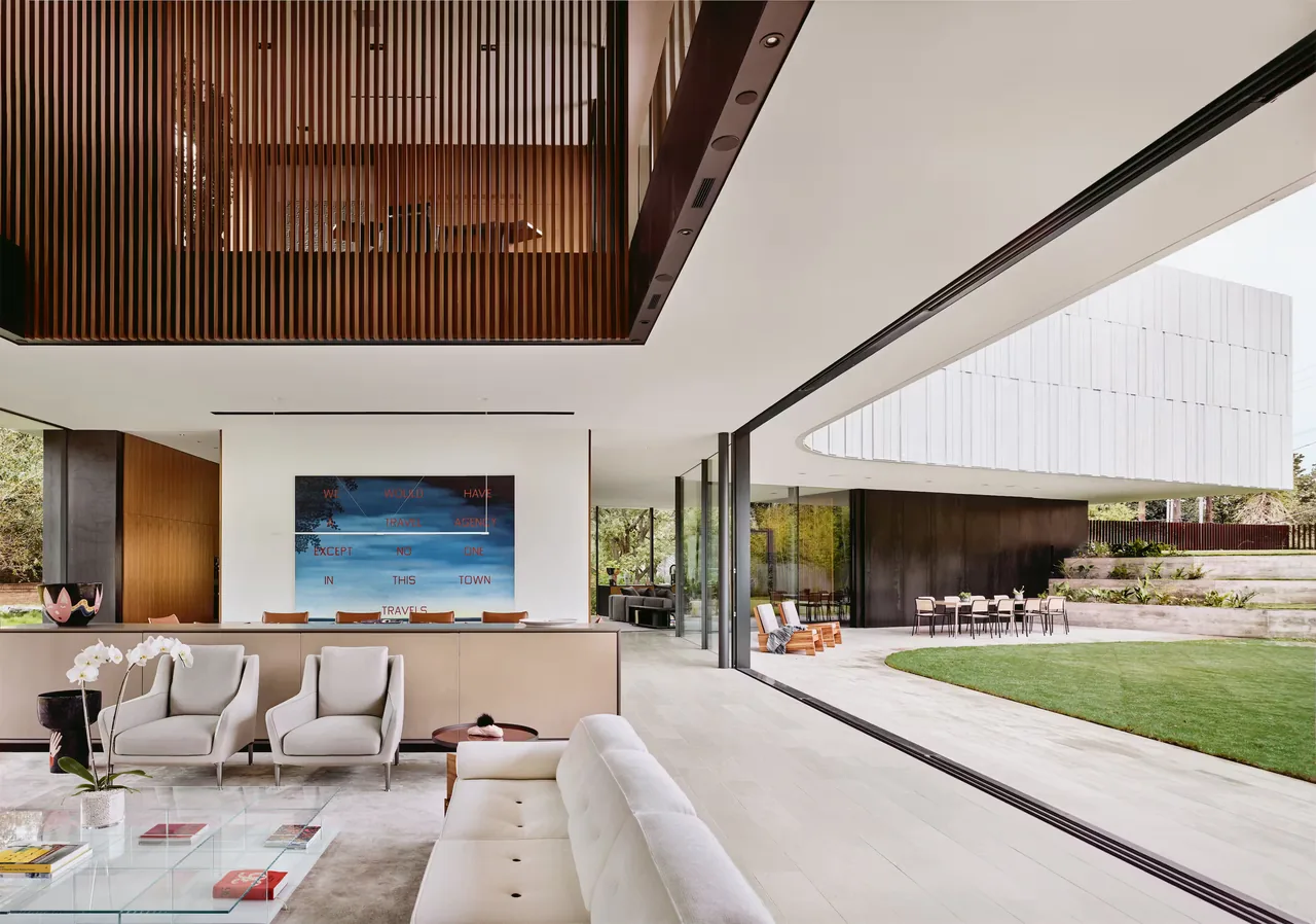 Highland Park Residence features a living room with floor-to-ceiling glazing opening to a covered patio and landscaped garden.