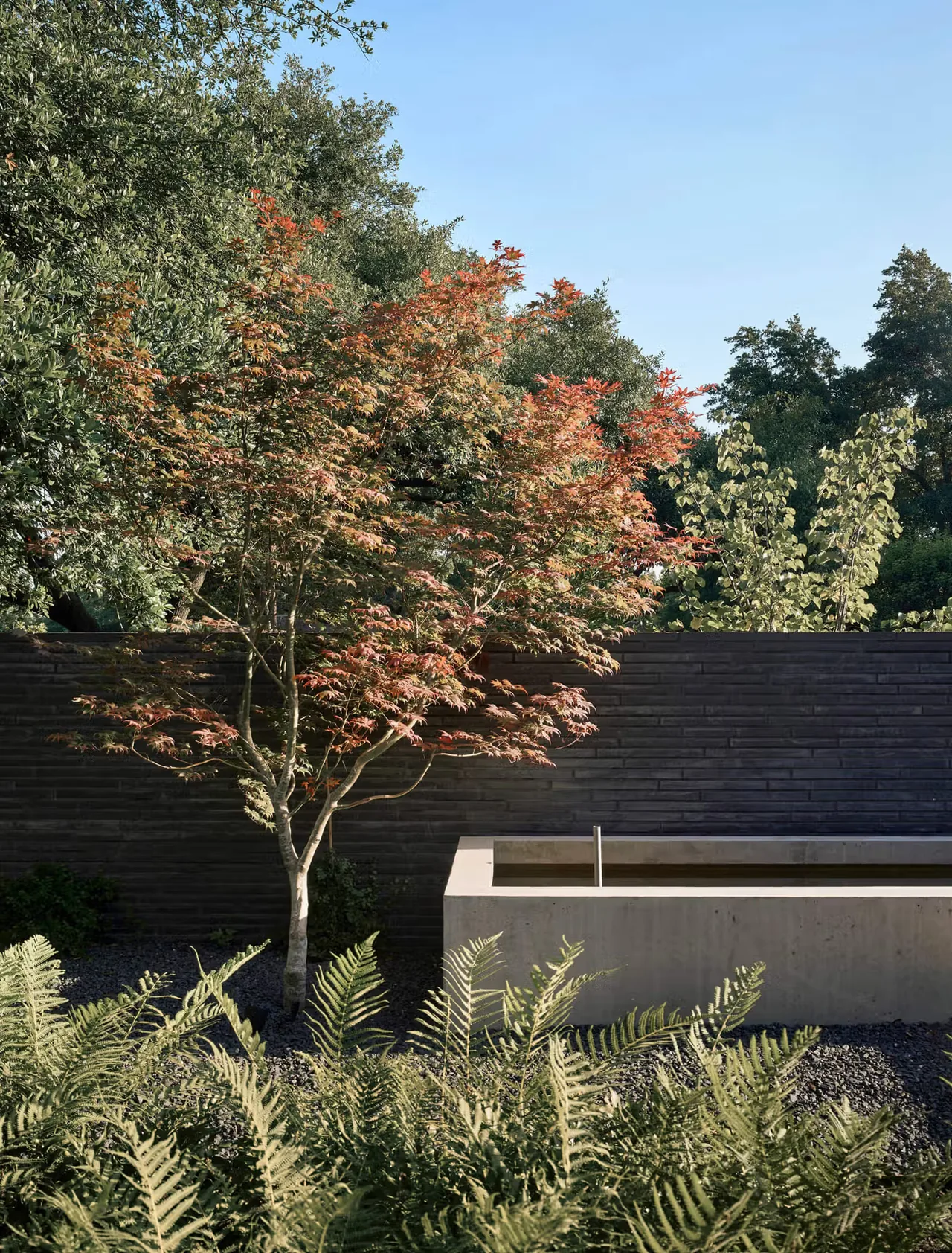 A garden water feature beside a black brick privacy wall with lush landscaping at Tarrytown Residence.