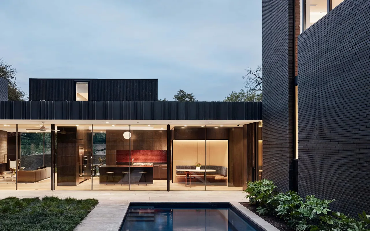 View of modern residence exterior with black brick walls, floor-to-ceiling windows, and a pool surrounded by landscaping.