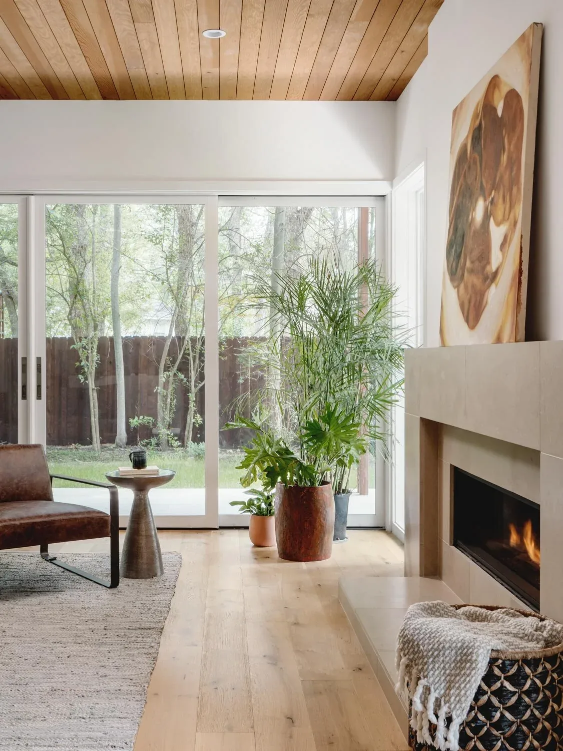 Living room in the Crestvale residence features a wooden ceiling, modern fireplace, and large windows with views of a wooded backyard.