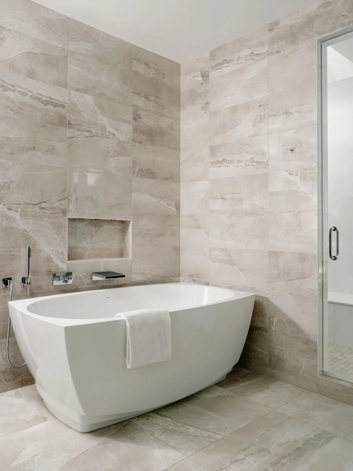 Bathroom features a white freestanding tub surrounded by beige marble tile on walls and floor.