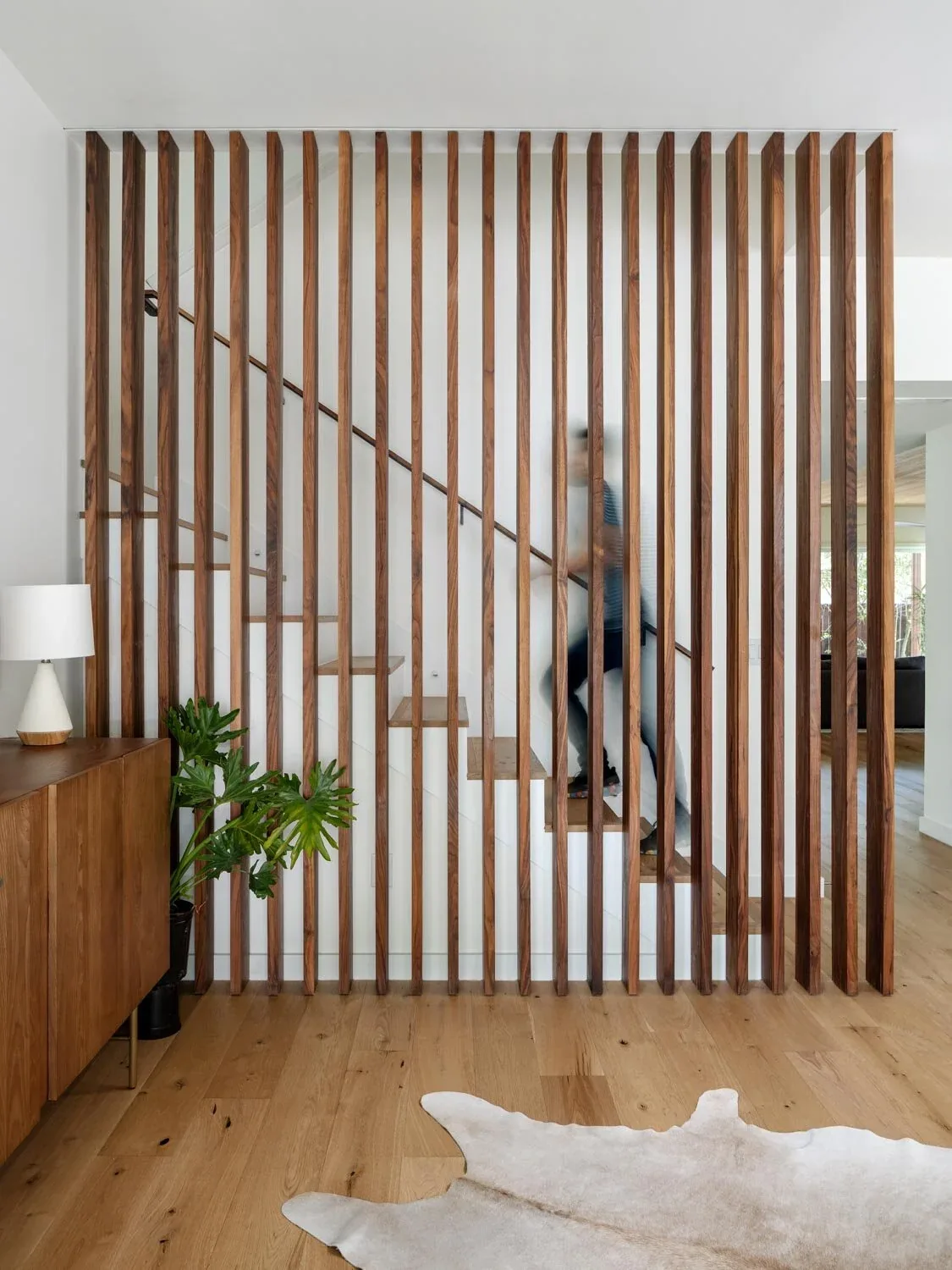 Interior view of a vertical wood slat partition separating a floating stair in a modern home.
