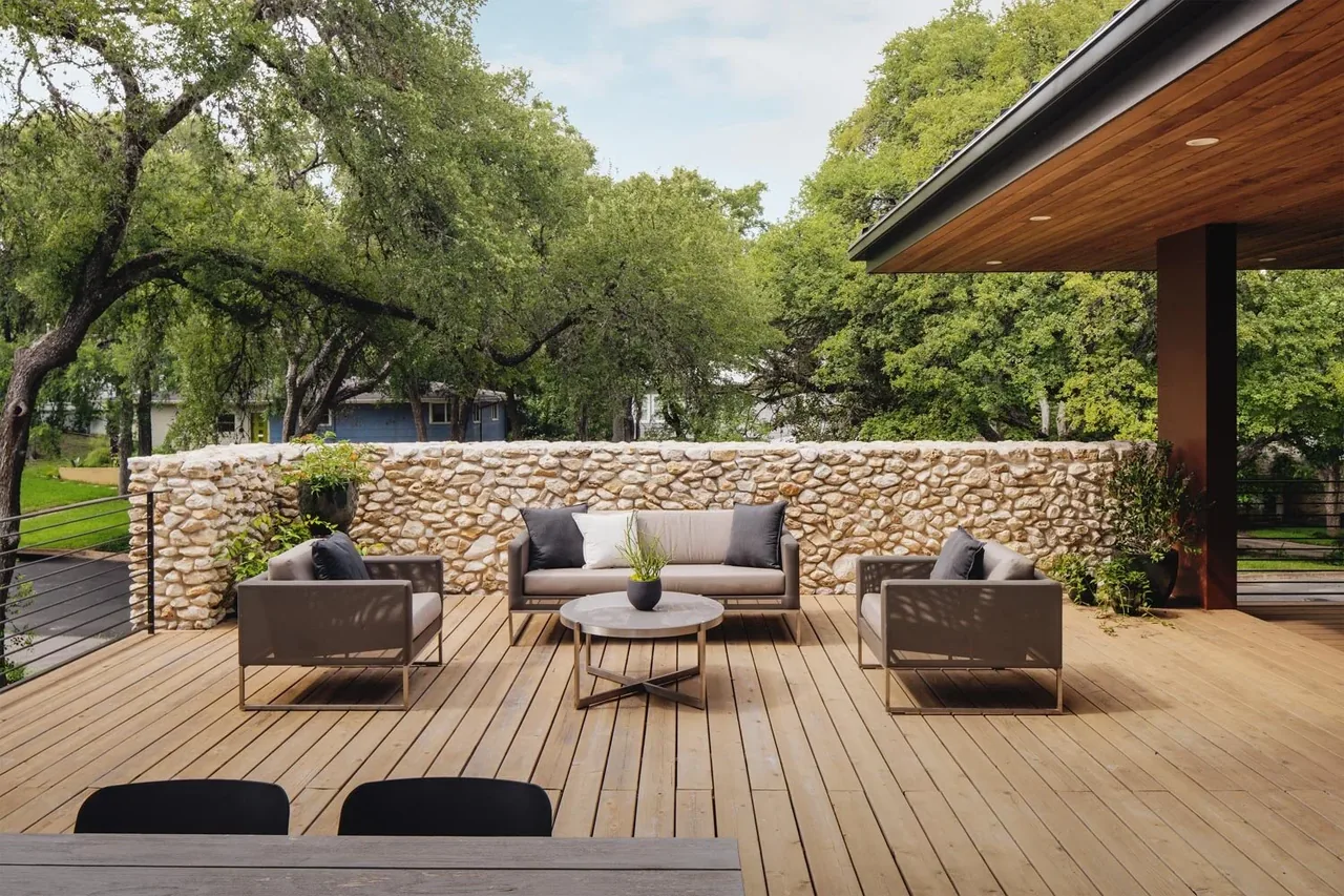 The Crestvale residence features a wooden outdoor deck with a stone privacy wall and modern gray patio furniture.