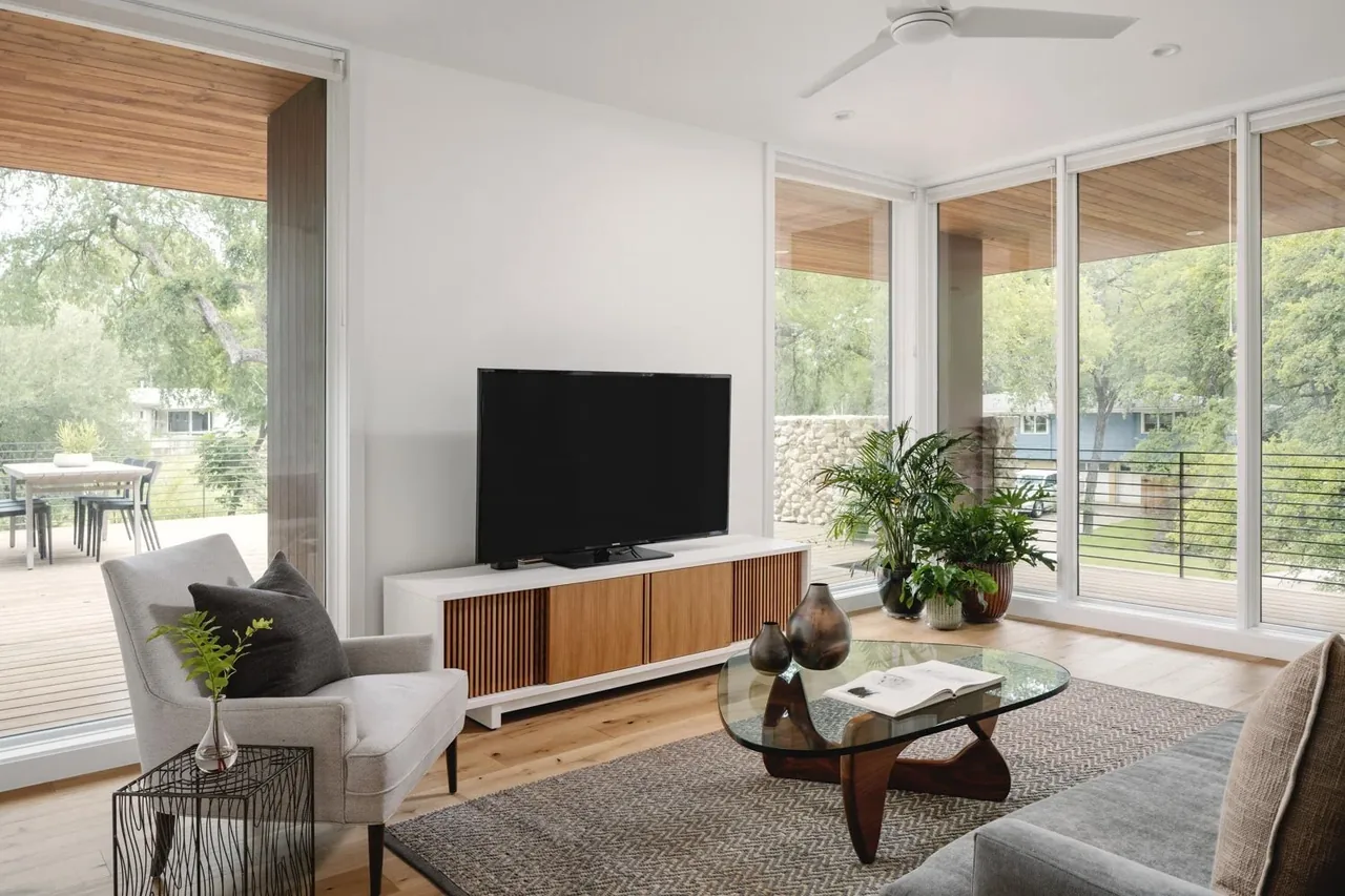 Living room with large glass sliding doors overlooking a covered deck, featuring modern furniture and natural wood accents.