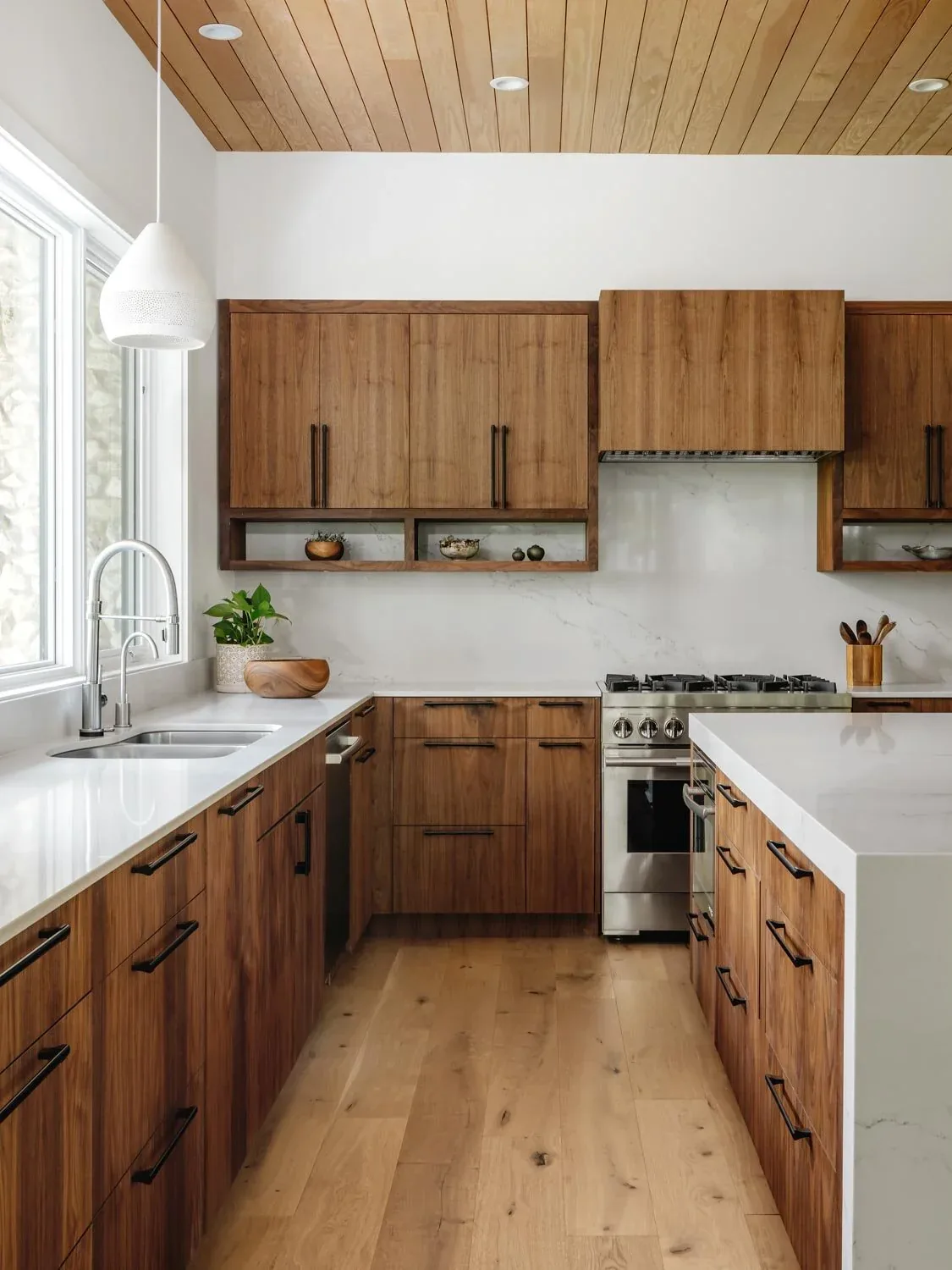 Crestvale Residence kitchen features walnut cabinetry with black handles, a white countertop island, and a stainless steel gas range.