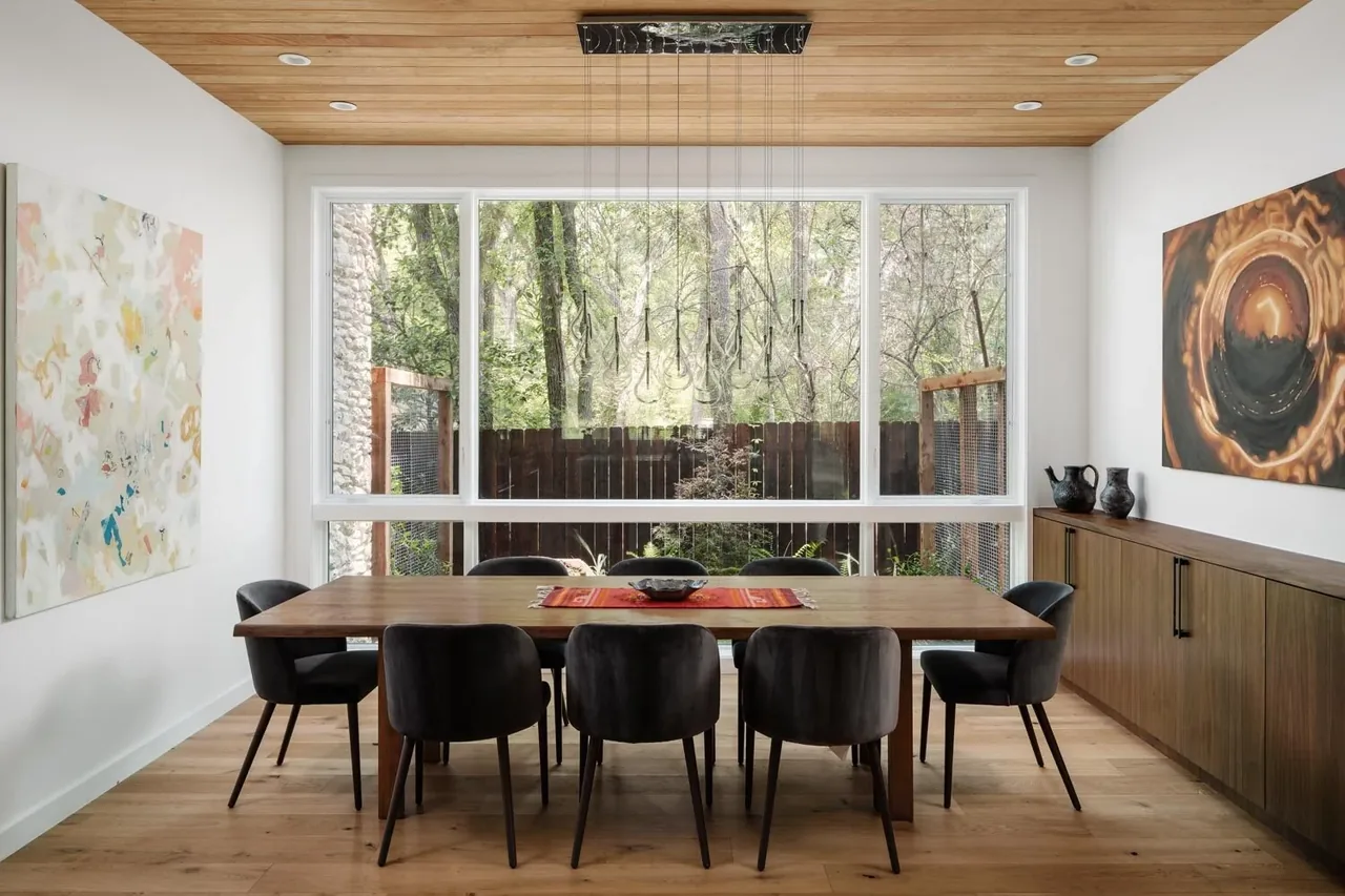Dining room features a large wooden table, six black upholstered chairs, and a wood-paneled ceiling with recessed lighting.