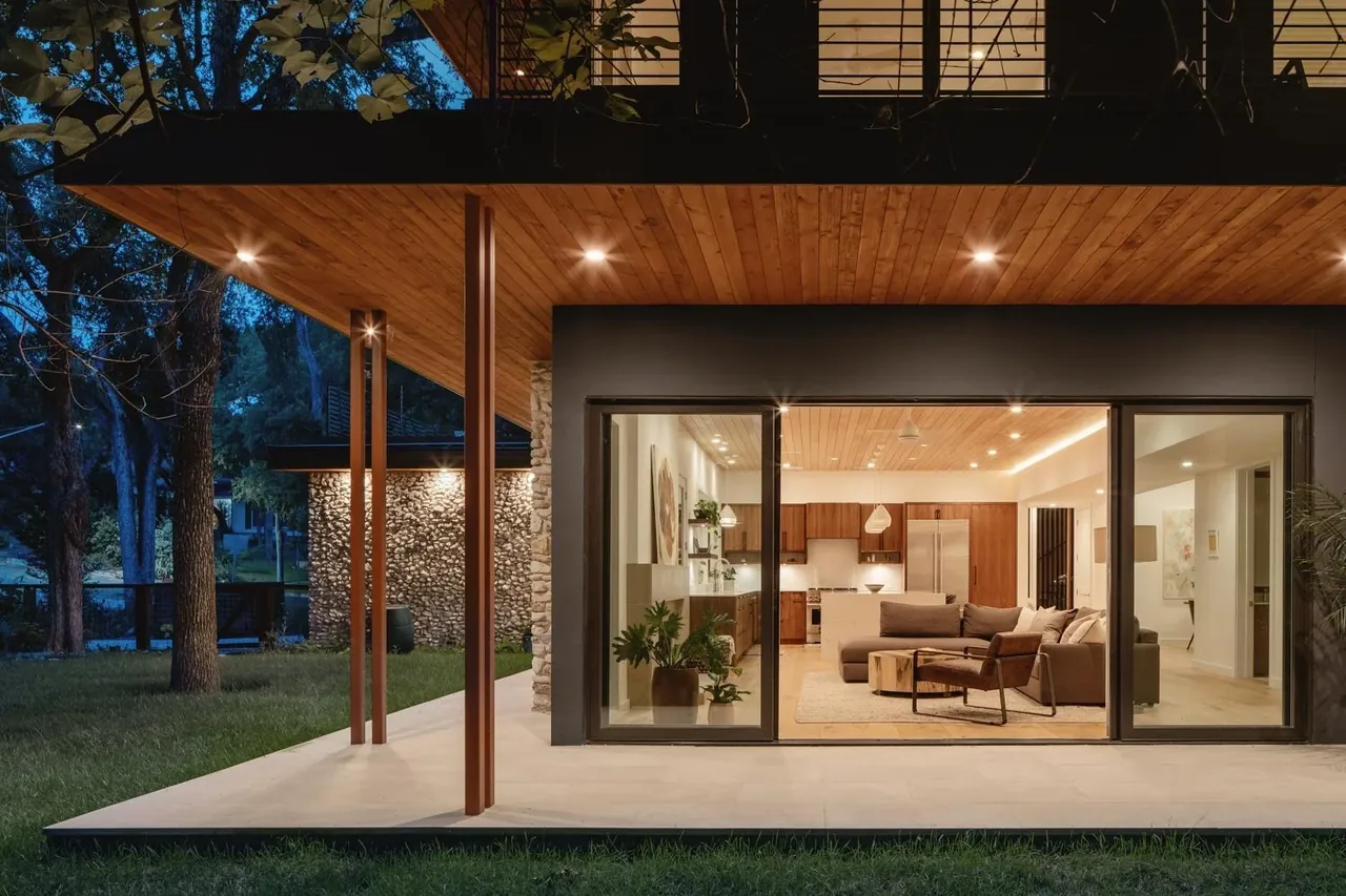 Crestvale Residence exterior showing wood soffit, stone cladding, large sliding windows, and covered patio at night.