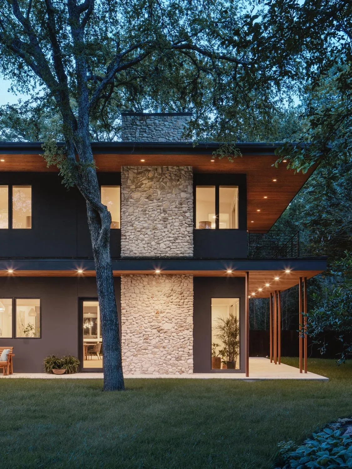 Crestvale residence by Clark | Richardson Architects features stone cladding, wood soffits, and a covered patio with lighting.