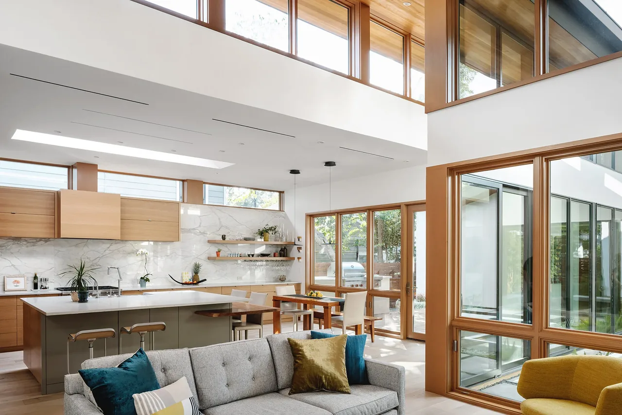 The Ramsey residence features an open kitchen and living space with large wood-framed windows and a wood-paneled ceiling.