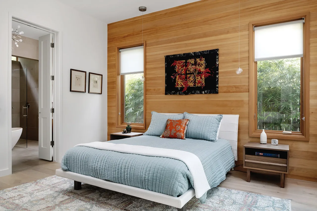 Bedroom with wood paneled wall, two narrow wood frame windows, and light blue bedding in Ramsey residence.