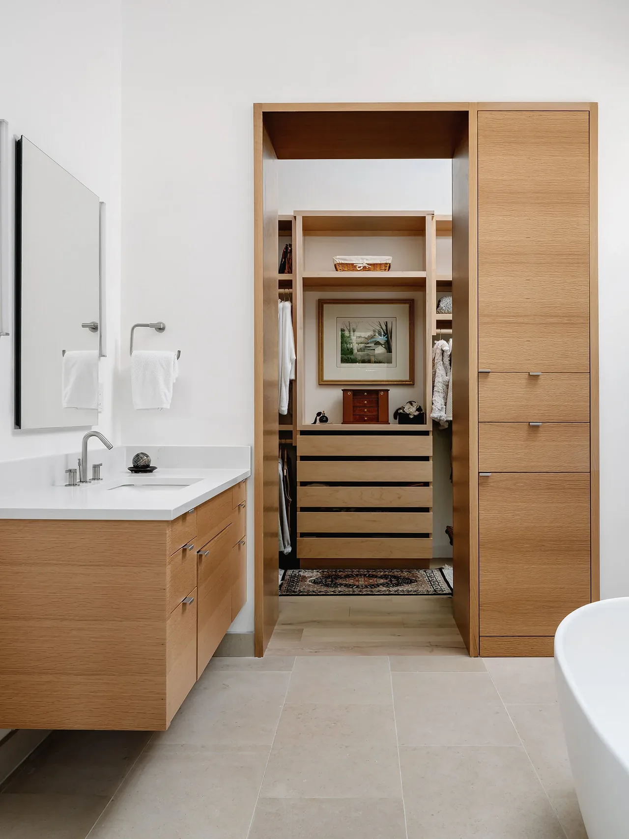 Bathroom featuring wood cabinetry and vanity with a view into a walk-in closet containing shelves and framed art.