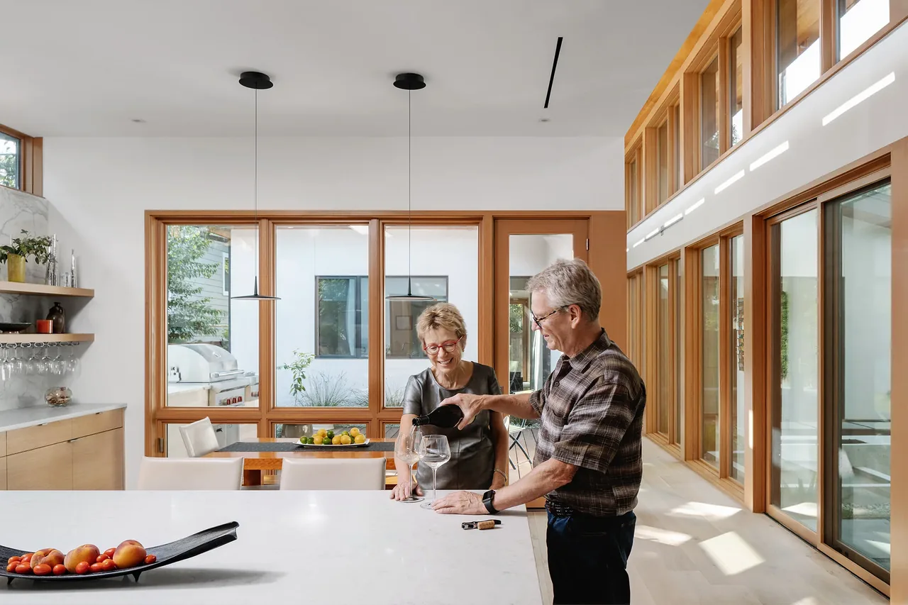 The Ramsey Residence kitchen features wood window frames, a white countertop island, and a dining table with pendant lights.