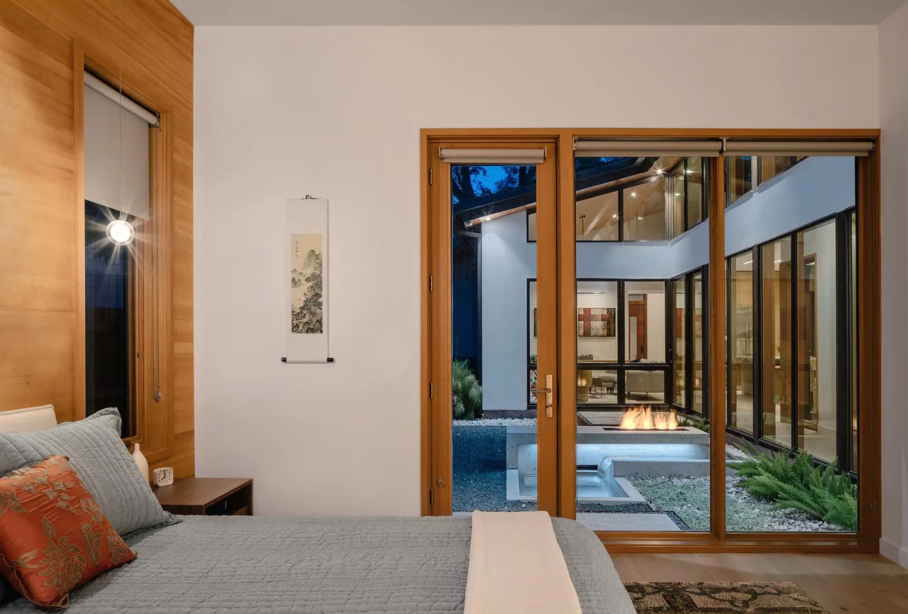 Bedroom of Ramsey Residence with wood-paneled window frames and sliding glass doors to courtyard with fire pit.