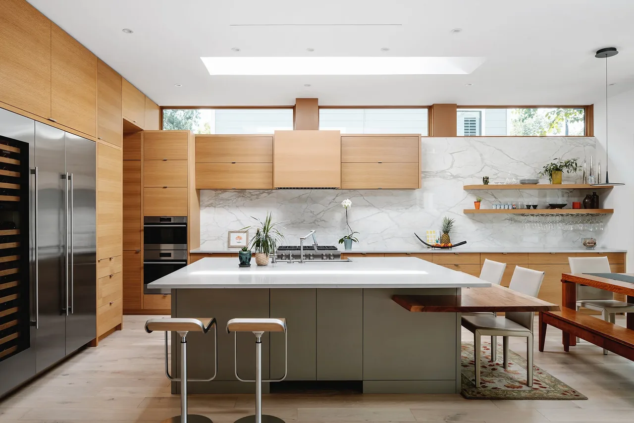 Ramsey residence kitchen features light wood cabinetry and marble surfaces with a central island and integrated seating.