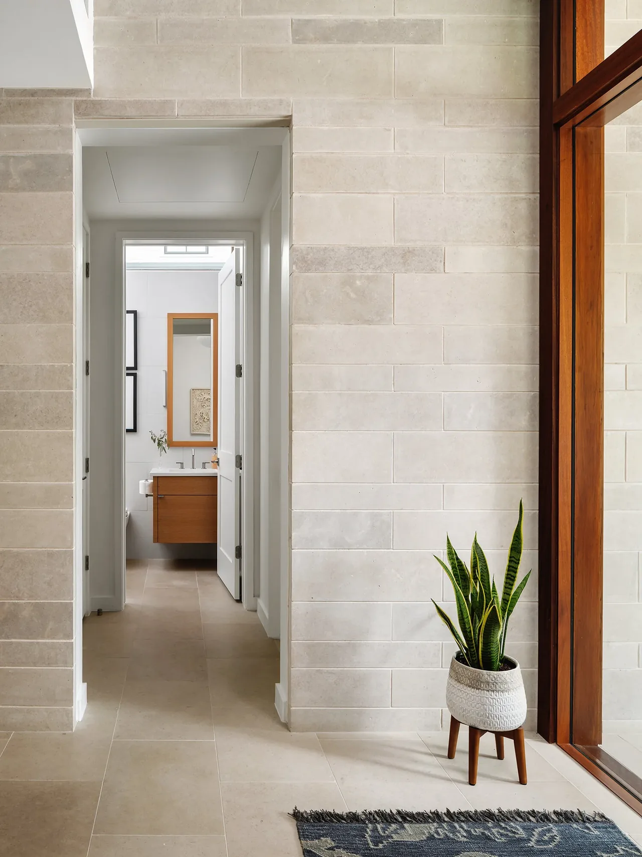 Hallway view into a bathroom with a floating wooden vanity and mirror in the Ramsey Residence.