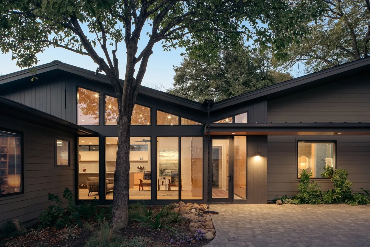 Modern butterfly roof home with black window frames and a rock drainage bed at the entrance.