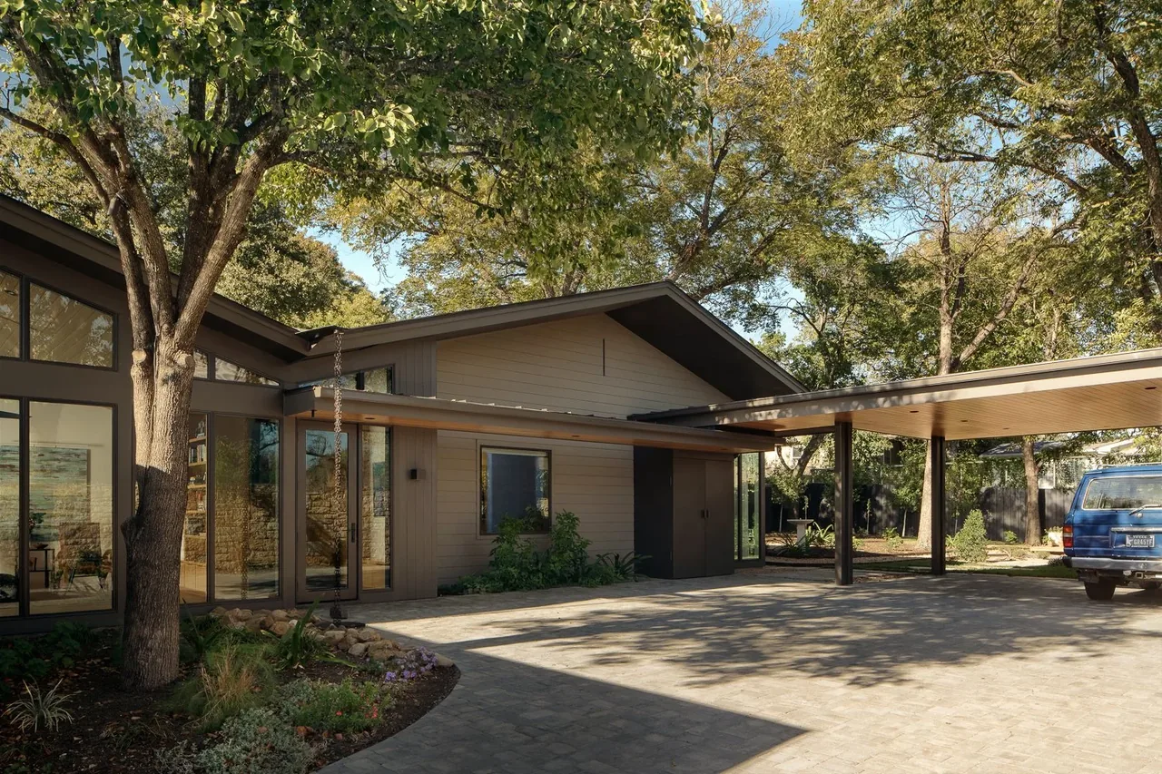 The butterfly residence features midcentury modern style with large clerestory windows and a carport in a natural setting.
