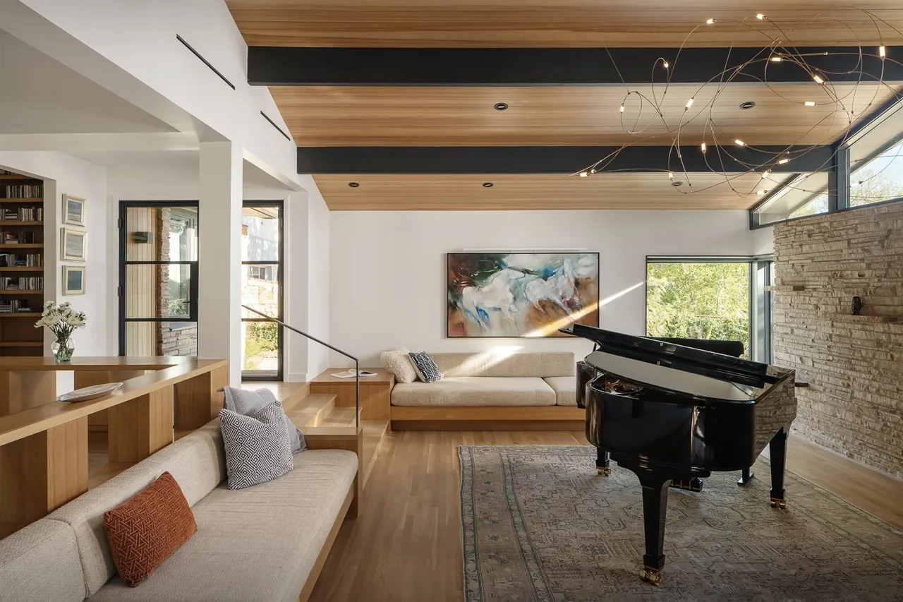 Living room featuring wood ceiling panels, a stone accent wall, built-in bench seating, and a black grand piano under a modern chandelier.