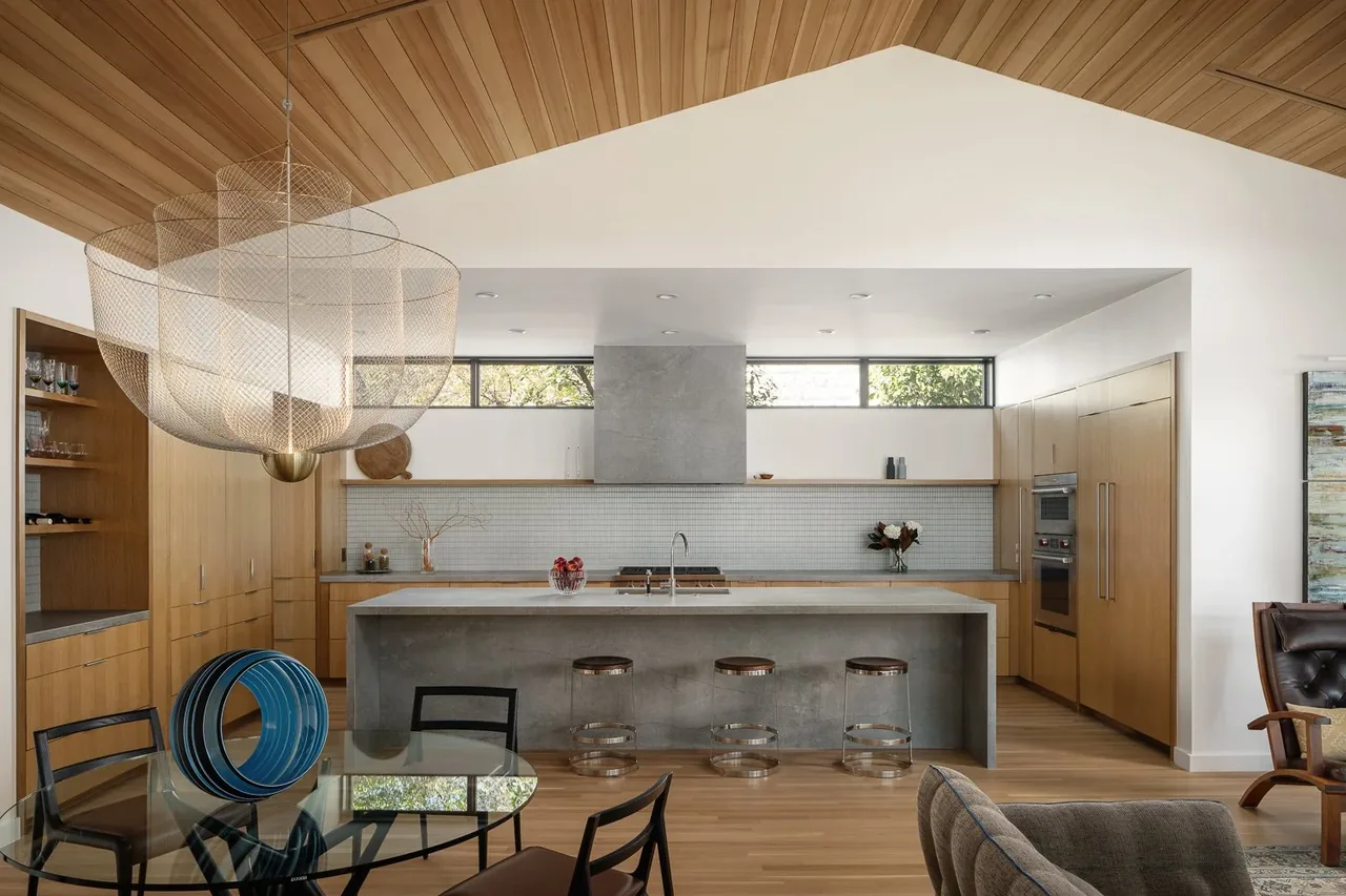 The Butterfly Residence kitchen features wood cabinetry and a concrete island under a vaulted wood-paneled ceiling with clerestory windows.
