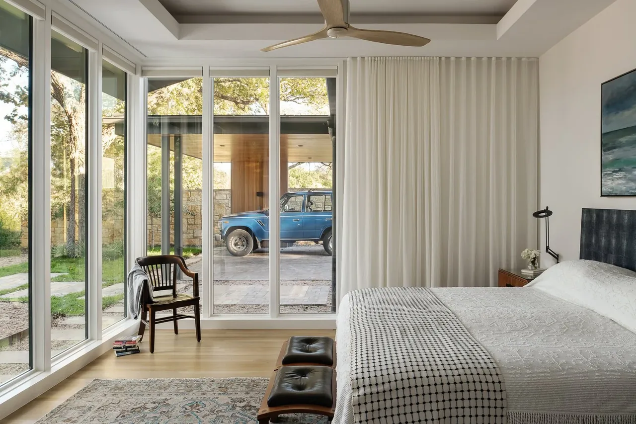 Bedroom featuring floor-to-ceiling glazing with views to a driveway and blue vehicle outside.