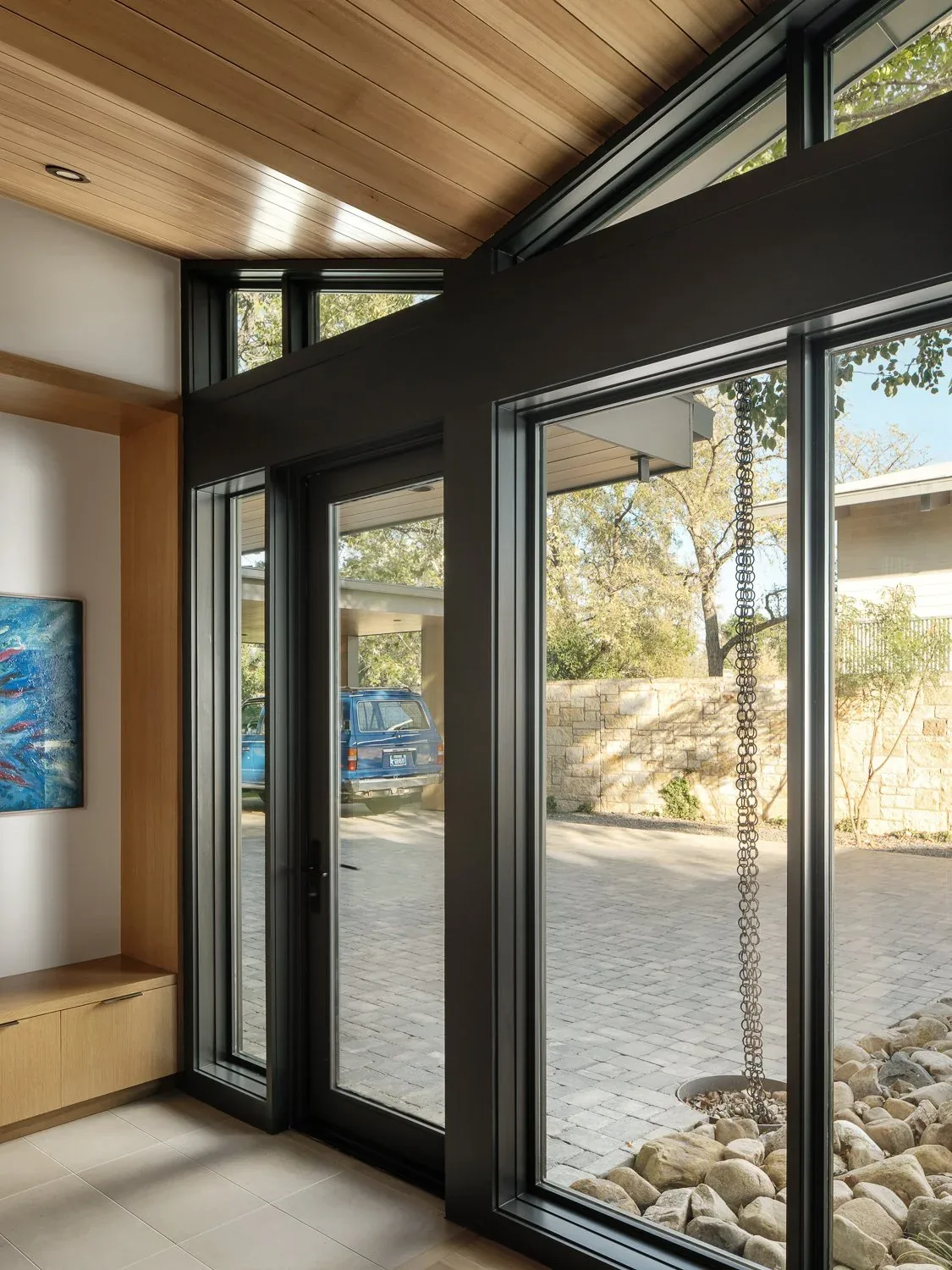 Room features black window frames, floor-to-ceiling glazing, and a wood-paneled sloped ceiling with clerestory windows.