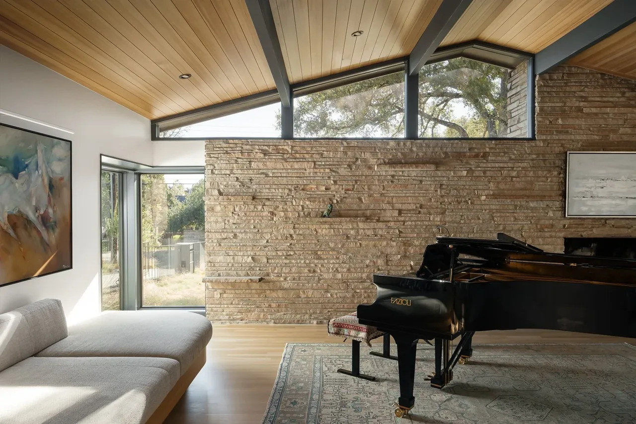 Living room in Butterfly Residence features a stone chimney wall, wood-paneled vaulted ceiling, clerestory windows, and a grand piano.