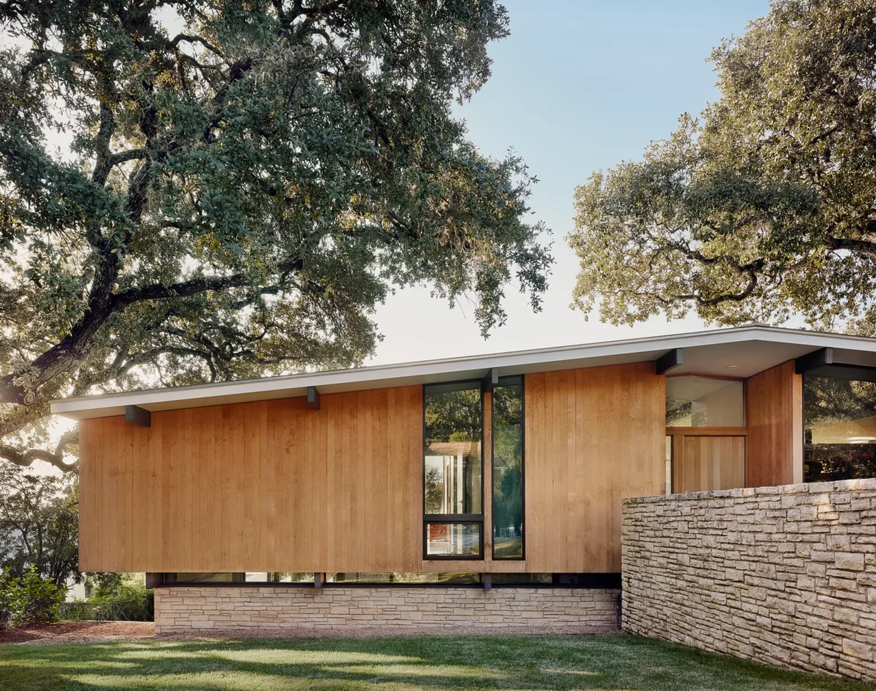 Wood and stone exterior of a modern house with a shed roof and large vertical window sections.
