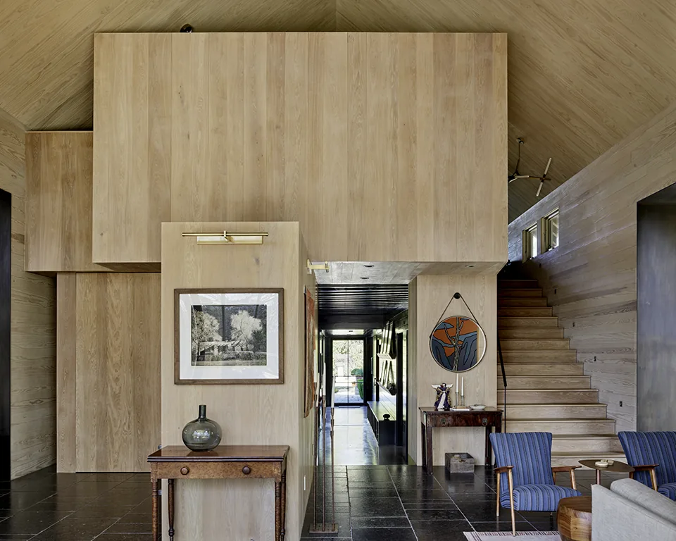 Hallway with wood-paneled walls and staircase, featuring vintage furniture and framed art.