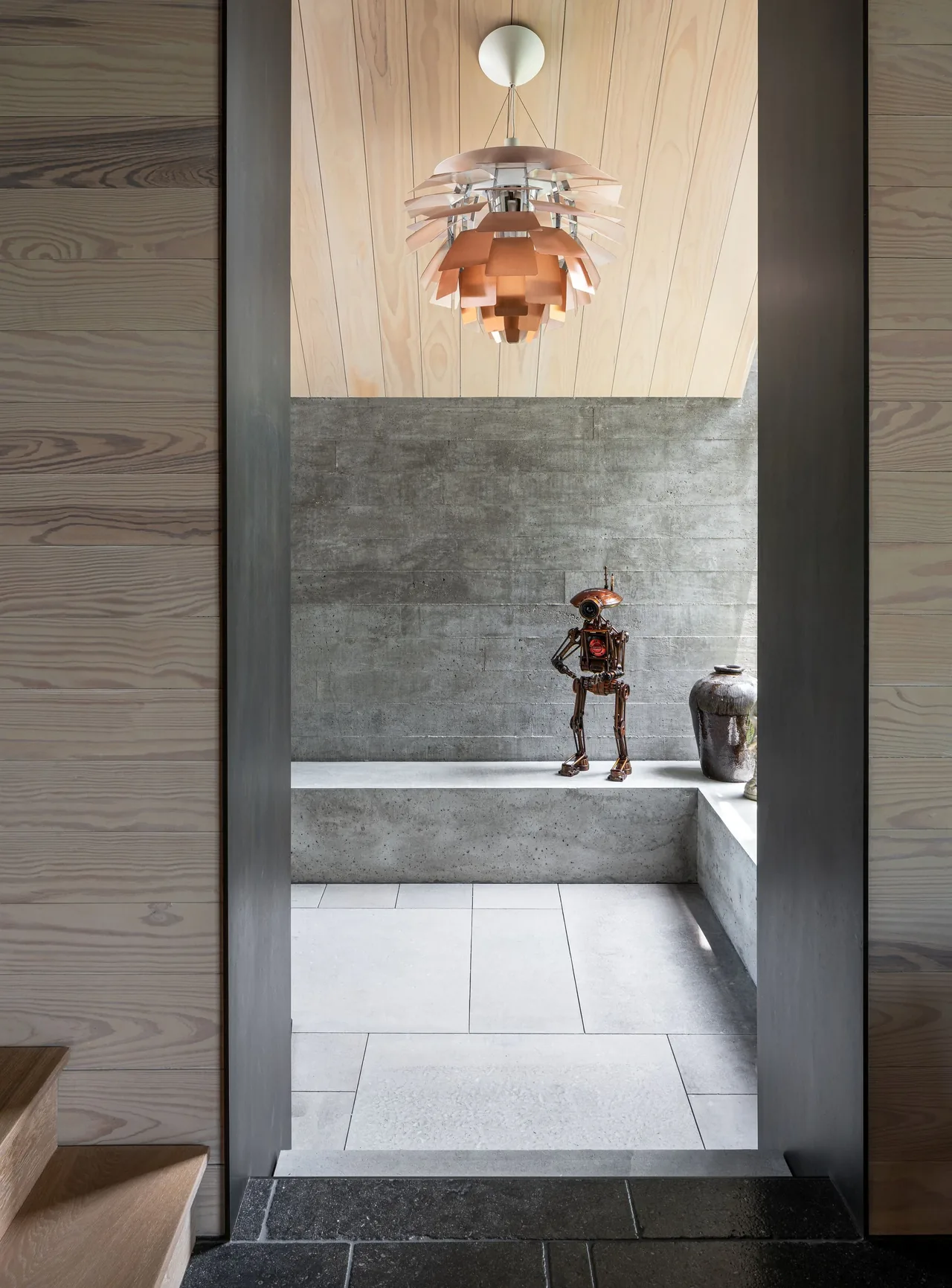 Concrete seating nook under a sloped wooden ceiling, featuring a modern pendant light and decorative sculpture.