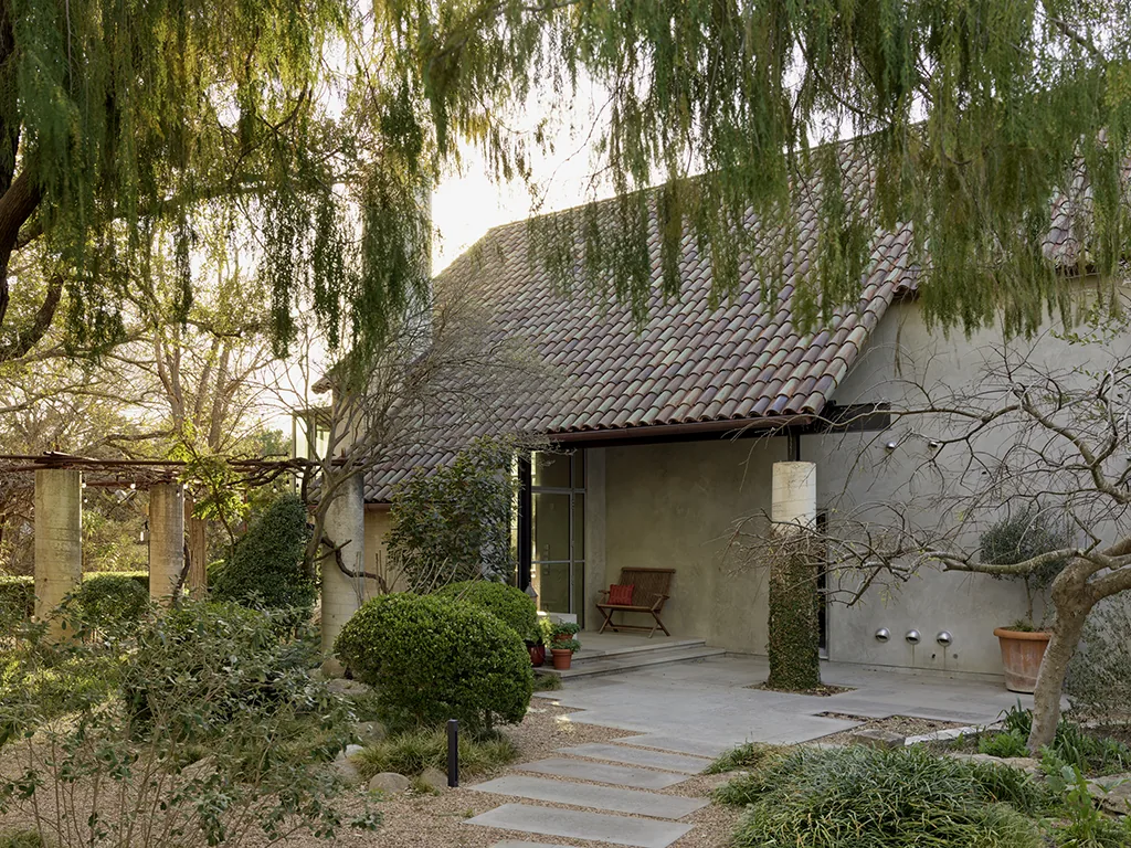 House entrance with clay tile roofing and concrete steps surrounded by manicured greenery in a garden setting.
