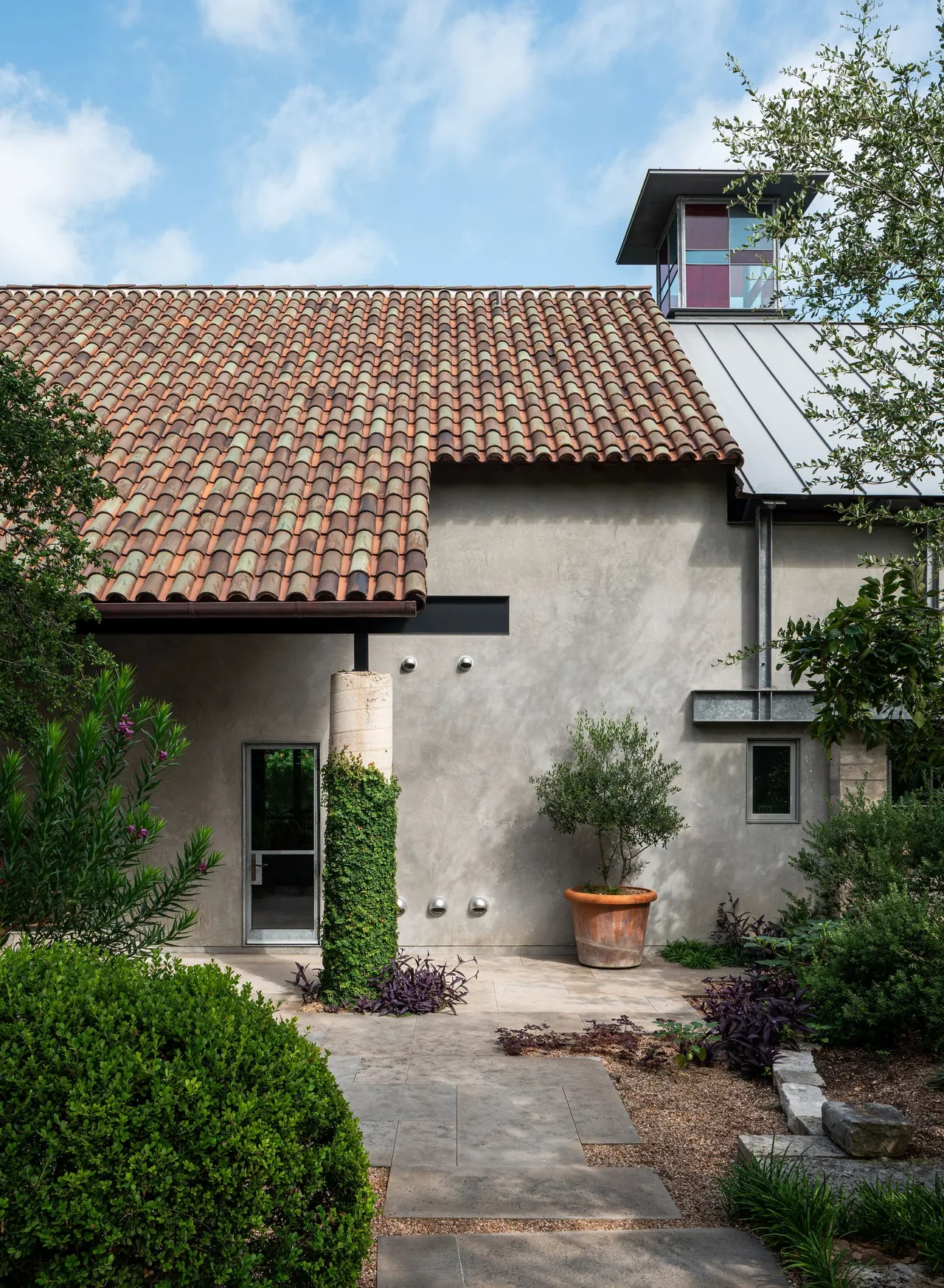 Hassell Gallery exterior showing the clay tile roof and stucco facade with greenery along the paved garden path.
