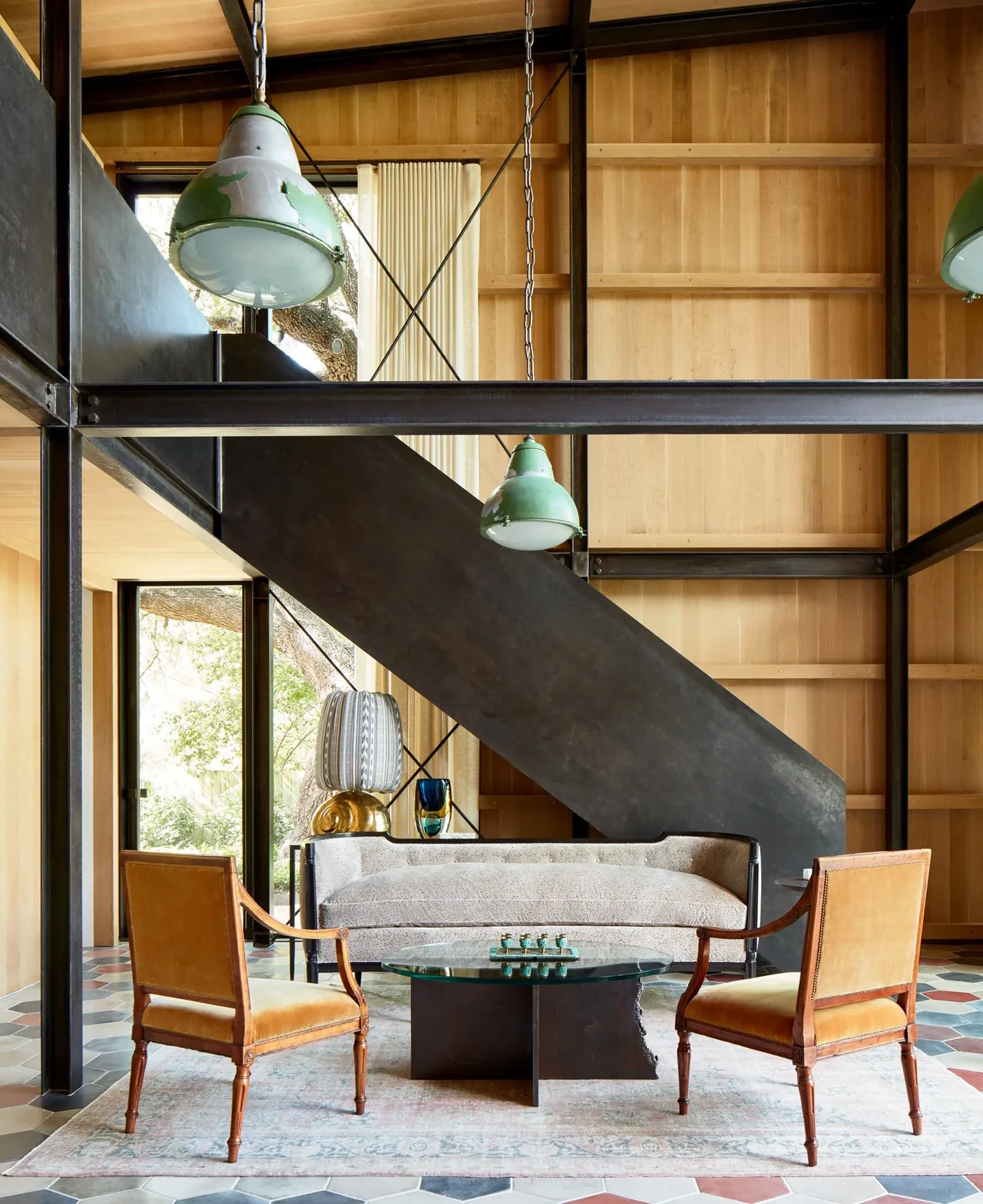 Modern living area features light wood walls, black metal staircase, and vintage-style furniture below green pendant lighting.