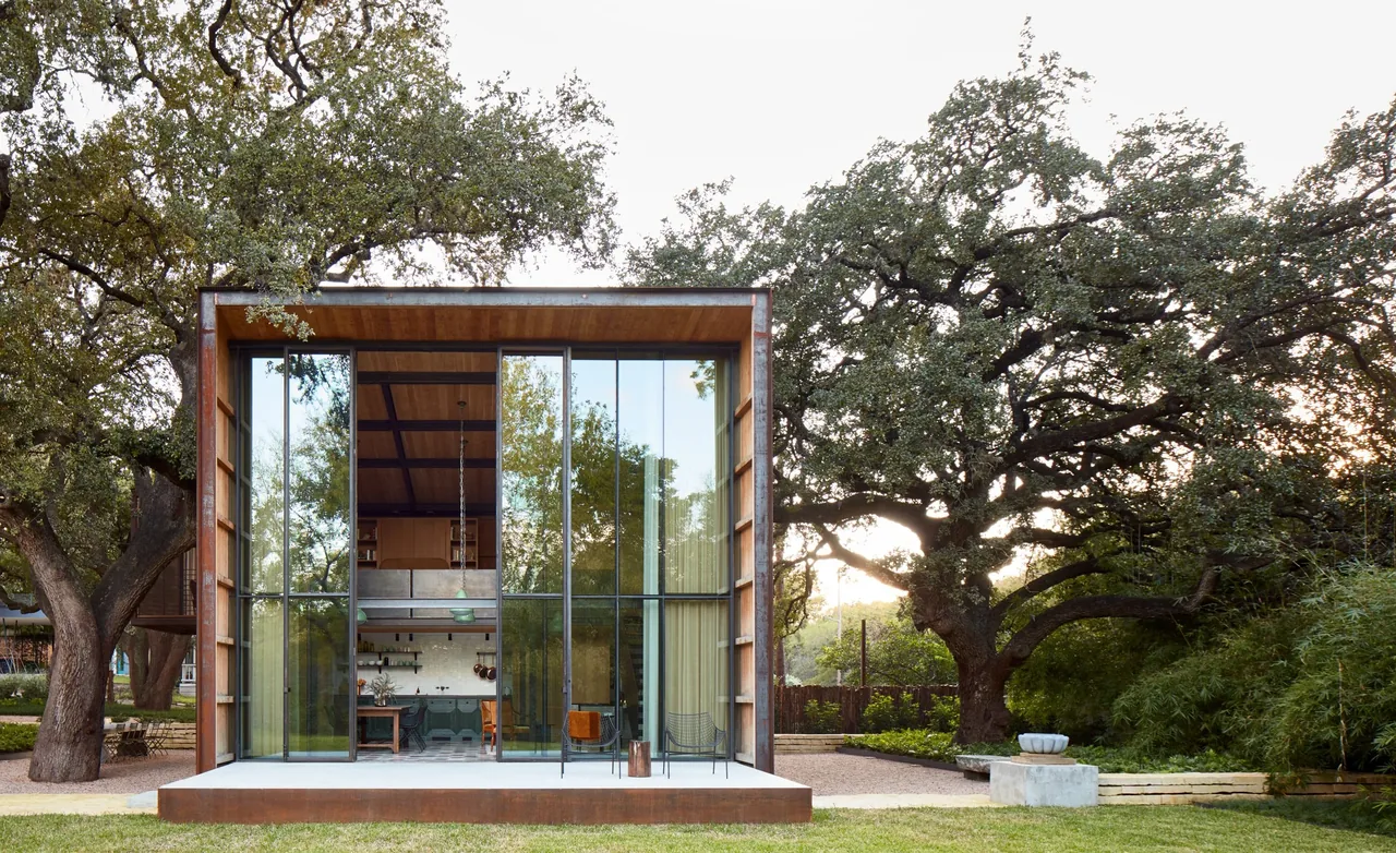 Jewell Box features a rust-patina steel framed exterior with floor-to-ceiling glazing facing a natural setting with large oak trees.